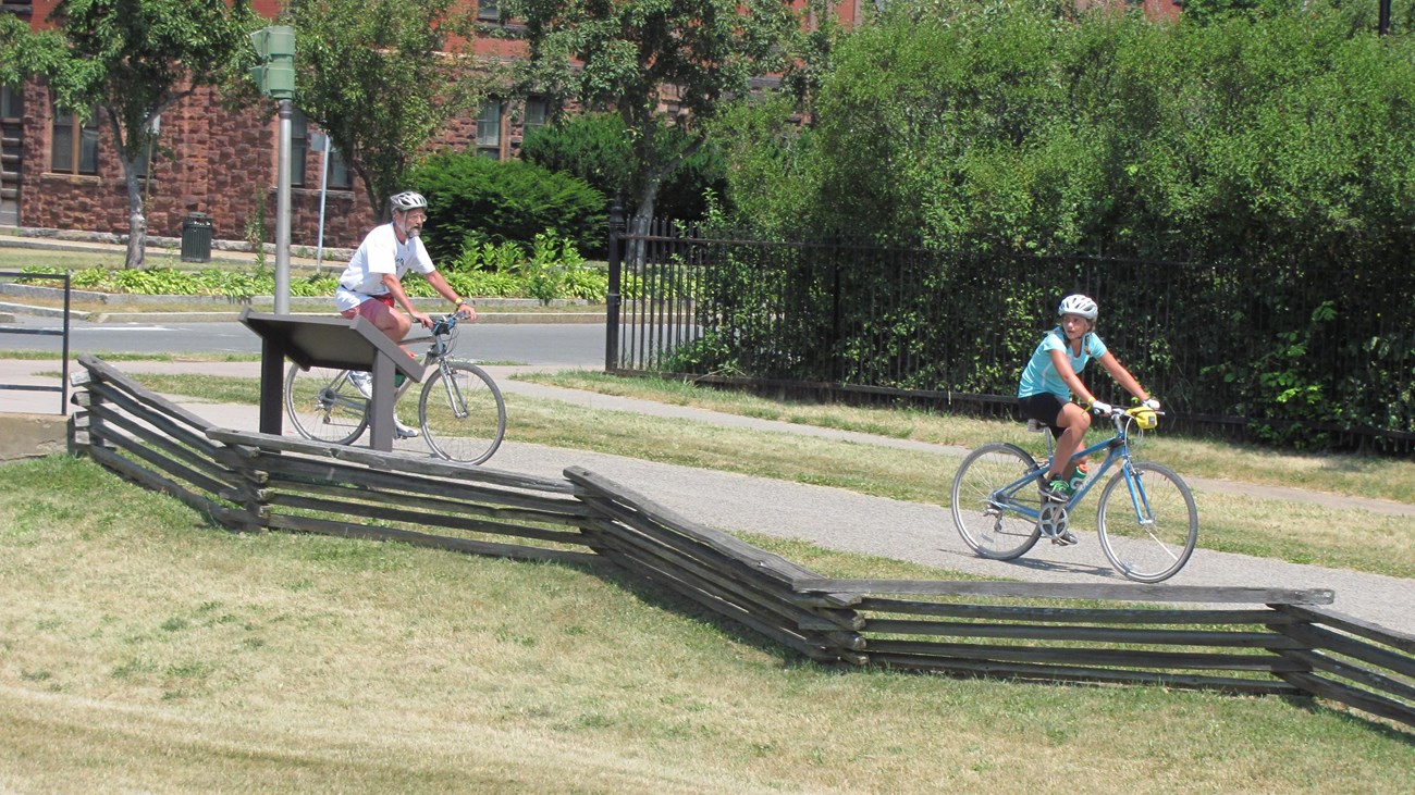 Two people cycle in a line down the park trail.