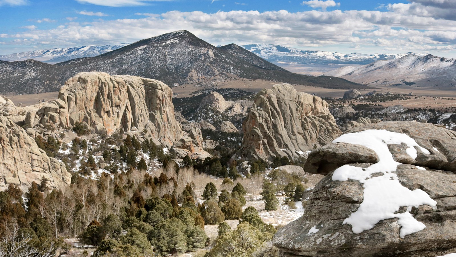 Grand scenic view of snowy granite formations and mountains in the distance.