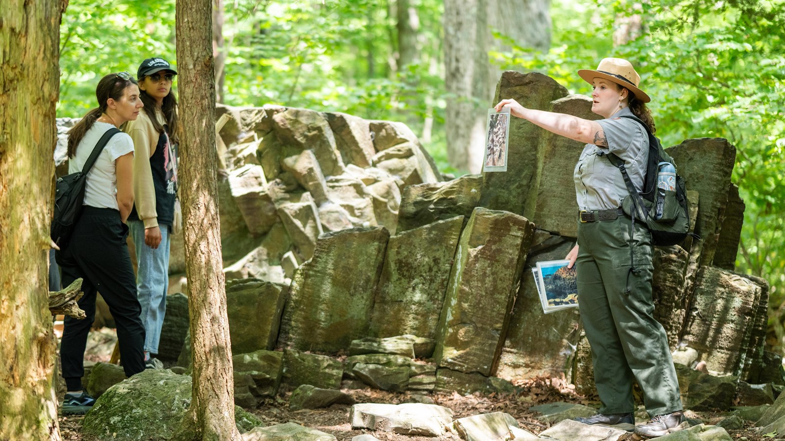 A ranger leads a tour and shows photographs in front of the columns of grey stone in the forest