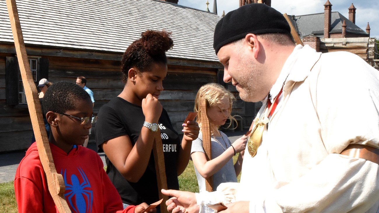 A boy stands opposite from a Continental Soldier, holding a wooden musket
