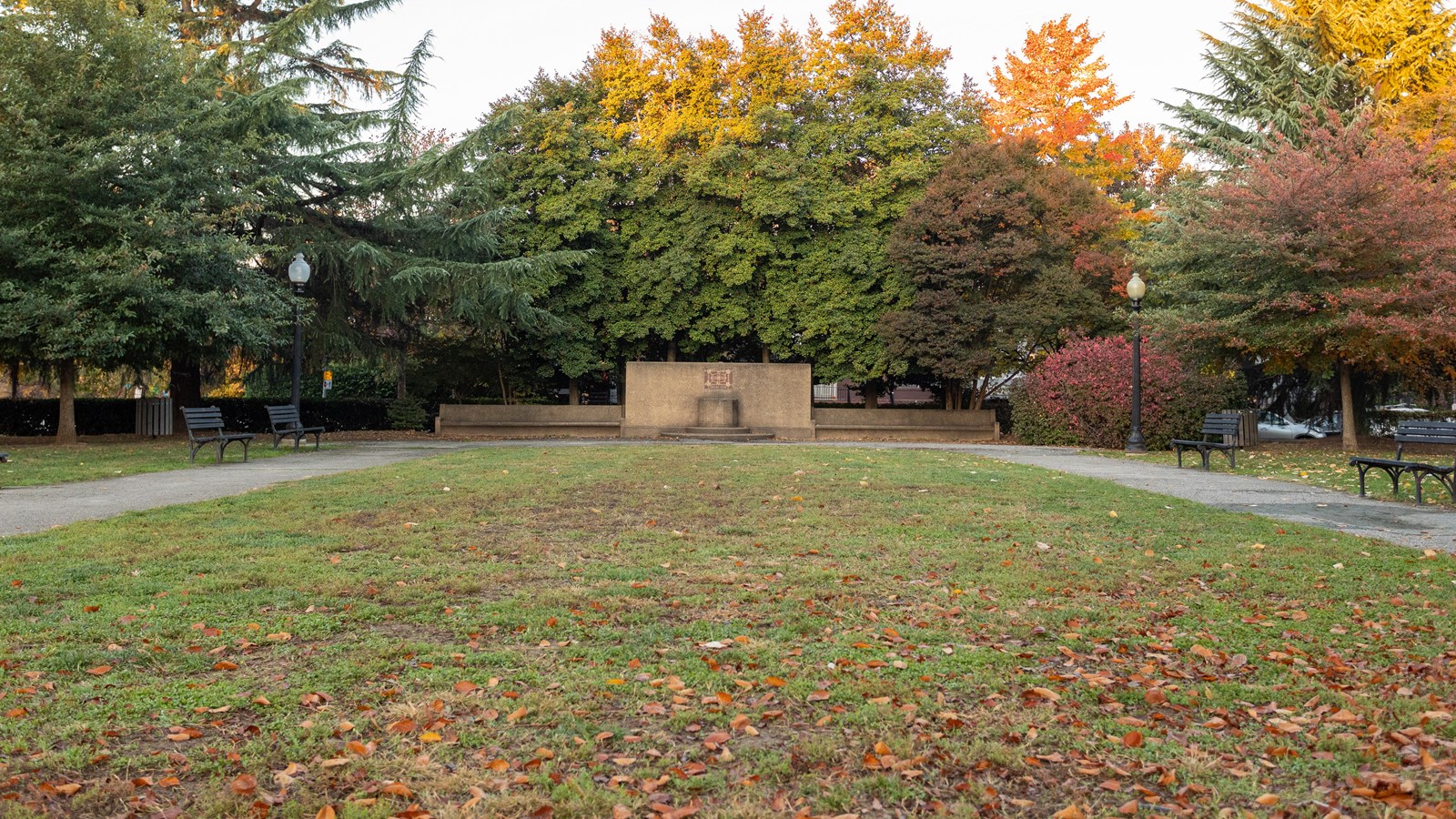 A long lawn is bordered by paved paths. A low, stone wall sits at the far end.