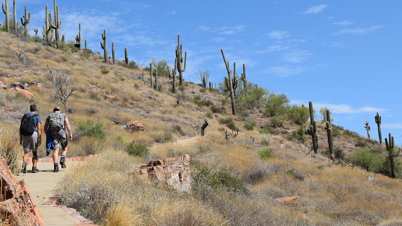 Two people walking up a steep paved trail through desert landscape.