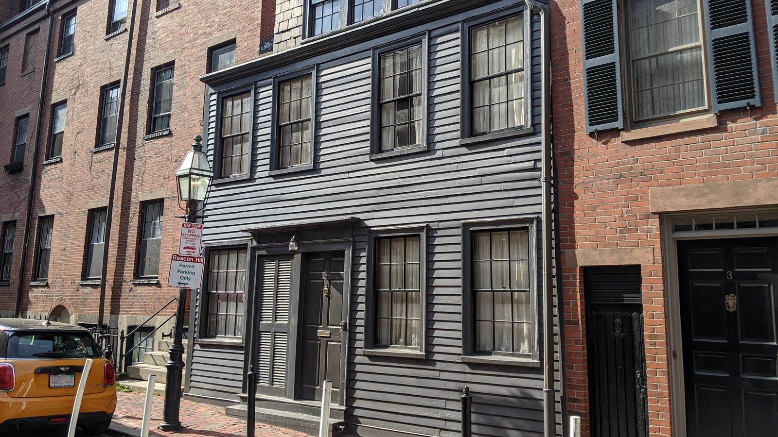 A two-story home with grey siding in between two brick buildings.