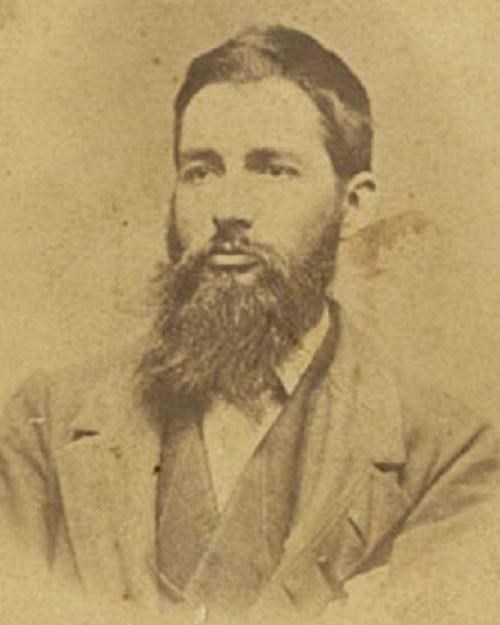 An 1800s portrait photo shows a long-bearded young man in a suit.