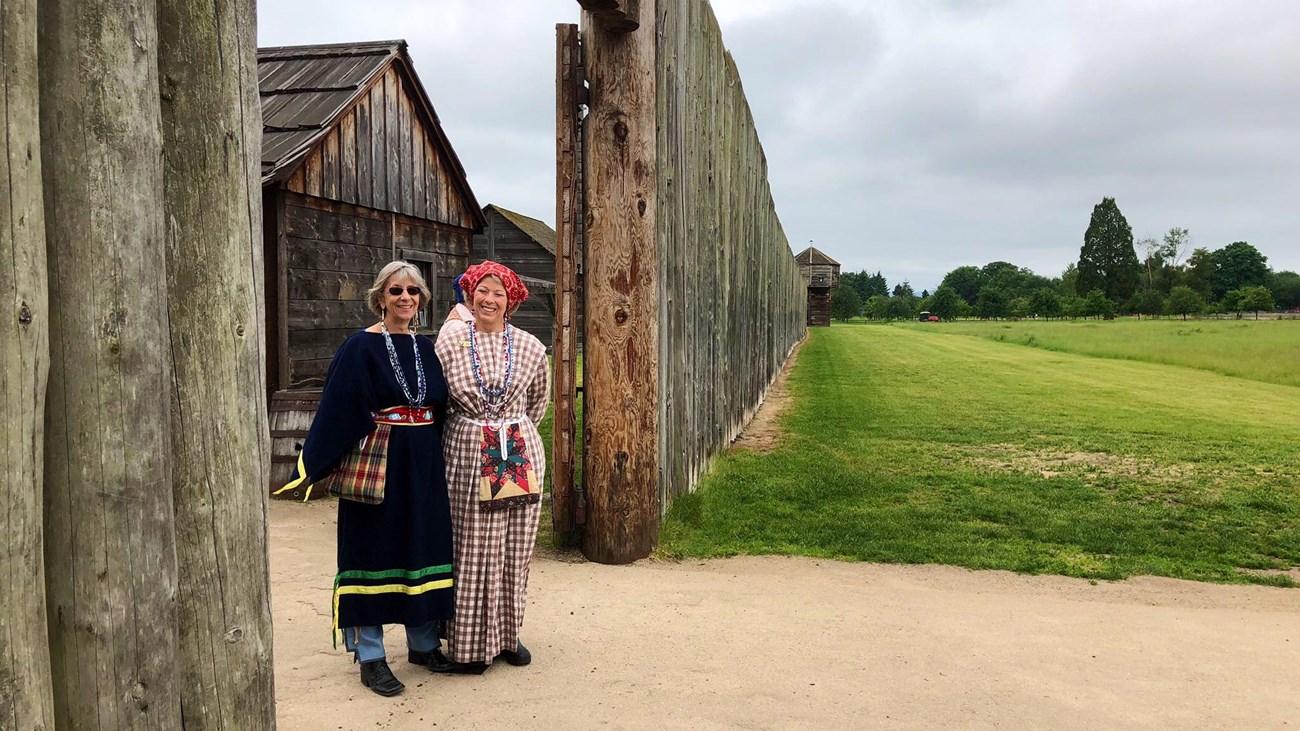 The gates of Fort Vancouver with two women in 1840s style clothing standing in front.