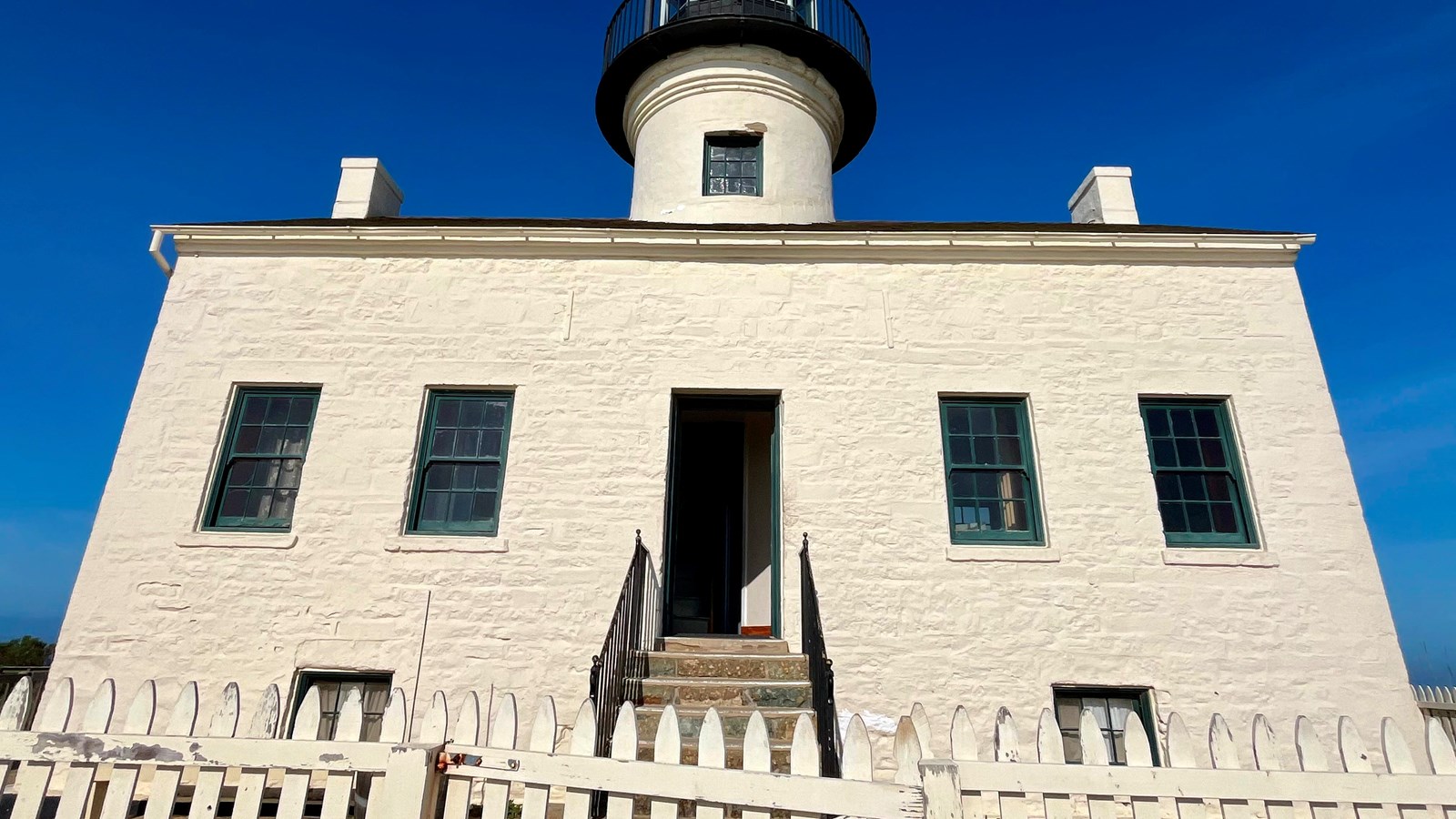 A white building with a white fence and stairs leading to a door. 
