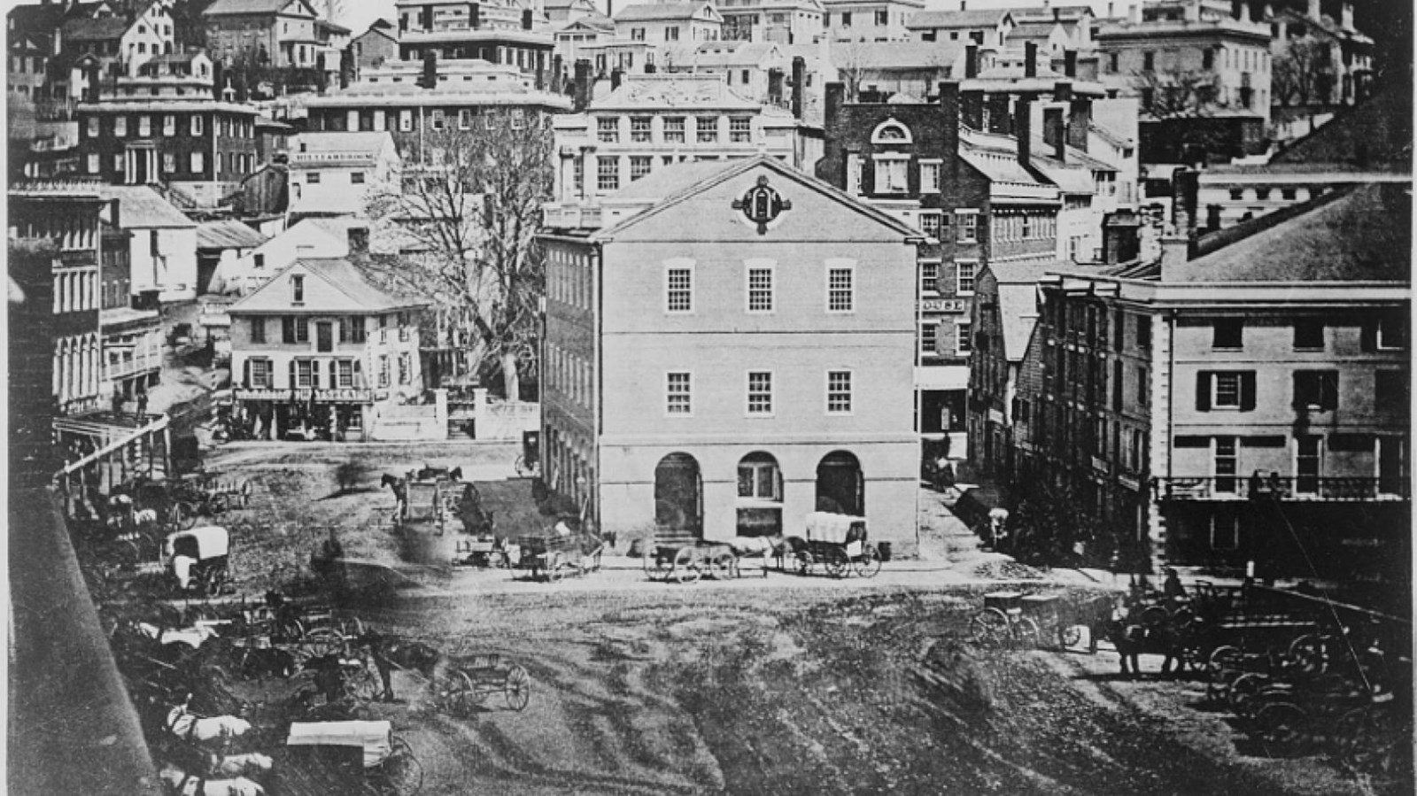 Three-story building surrounding by other structures. Open space in front of the building