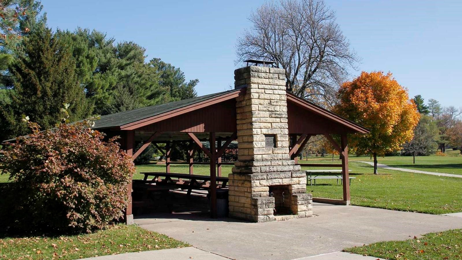 A timber picnic shelter has a limestone chimney and is painted reddish brown.