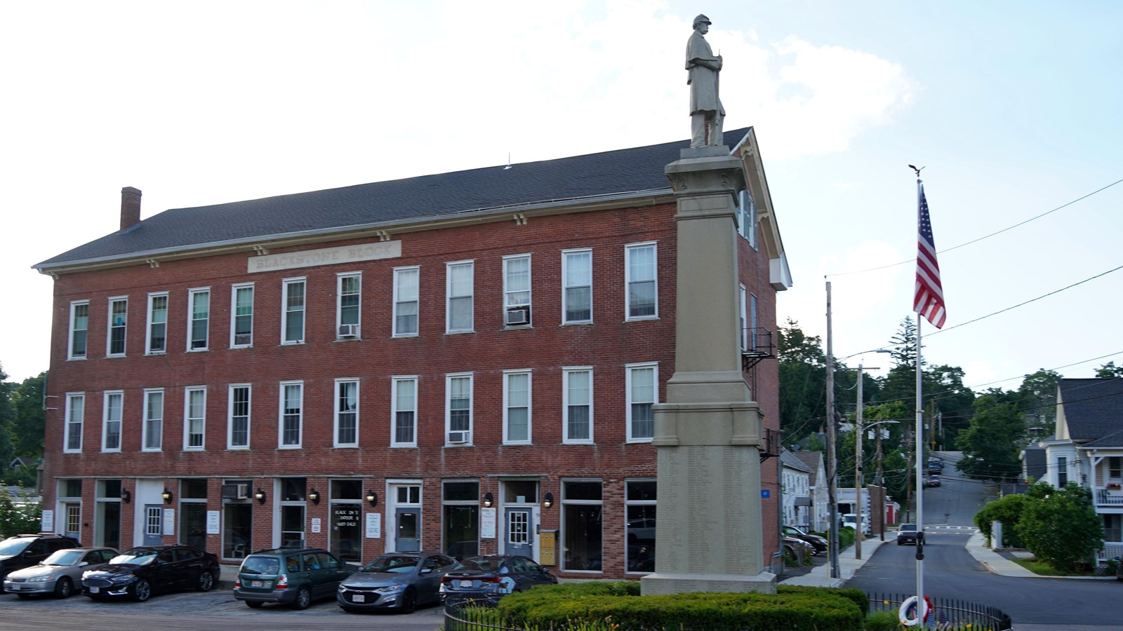 Large brick building with tall stone monument in front of it with soldier atop