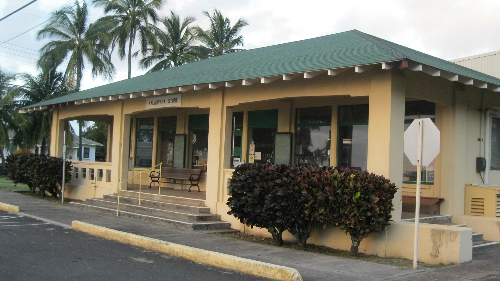 A tan building with a darker shingled roof. A sign out front reads Kalaupapa Store. 