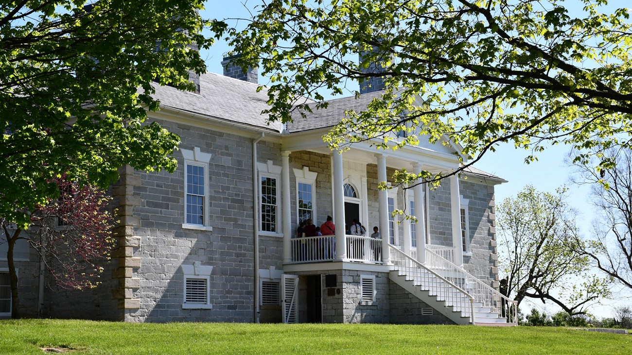 A tour group stands on the front porch of Belle Grove, a large limestone plantation house.