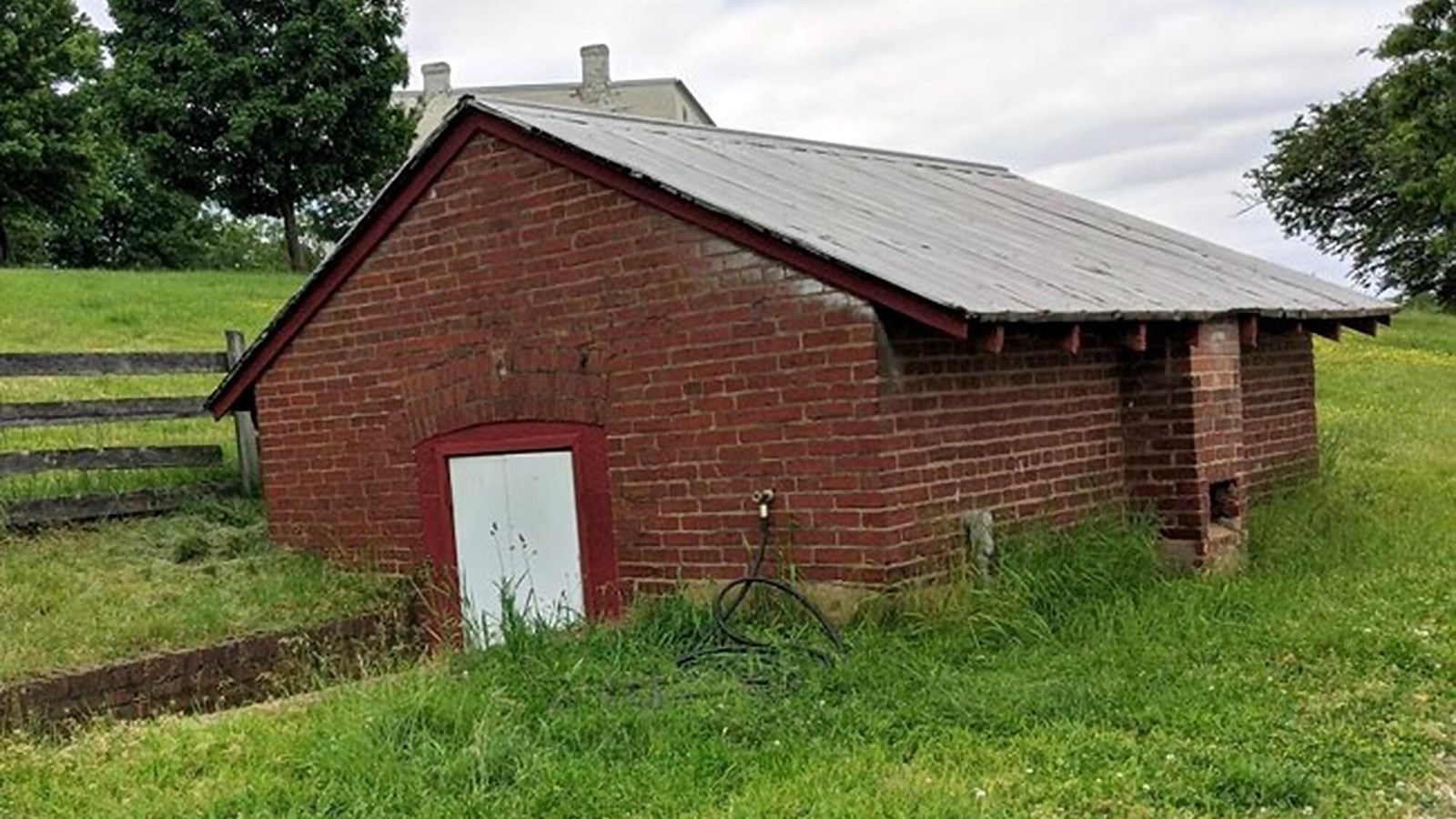 A small brick building with a grey metal roof sits partially below ground