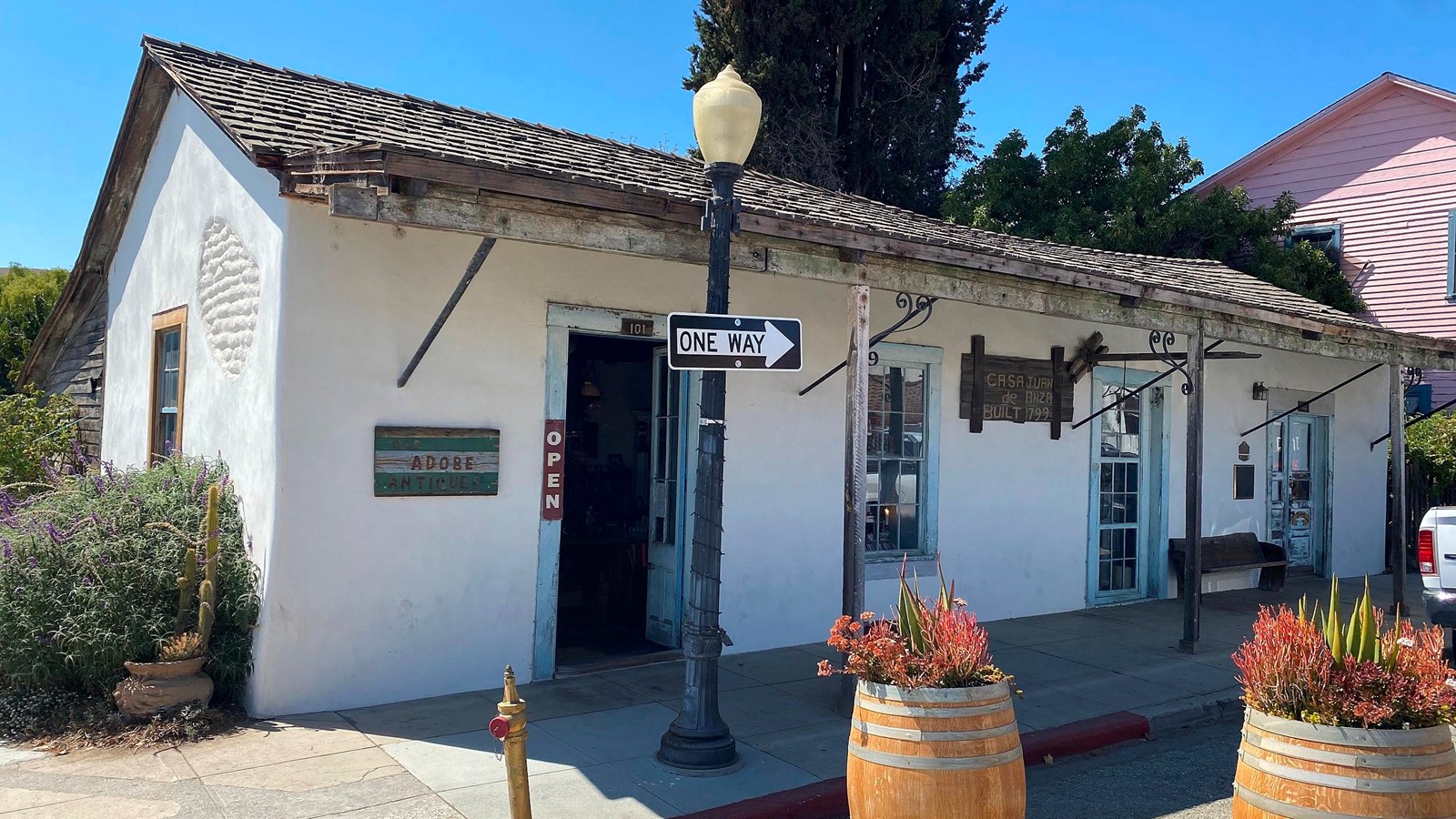 White single story adobe house with wood shingle roof and two doors and windows along the street.