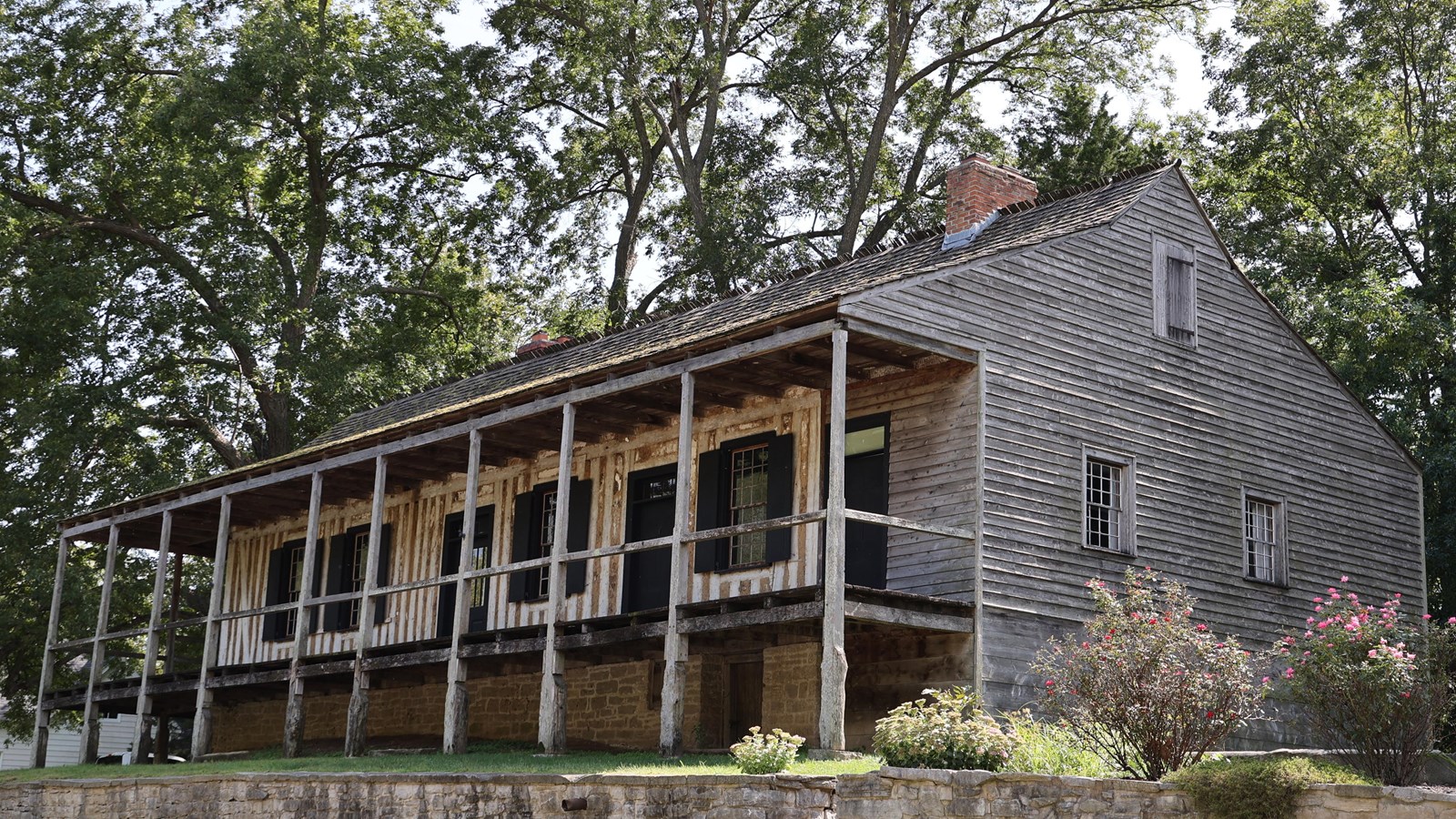 House with visible vertical log construction under covered porch, broken pitch roof and gables. 