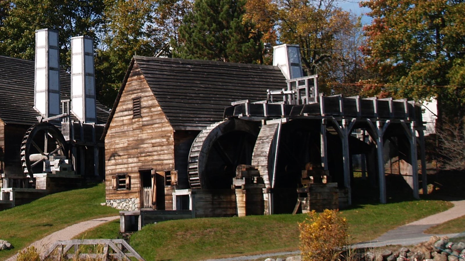 A wooden barn-like structure with two water wheels and a chimney in the back