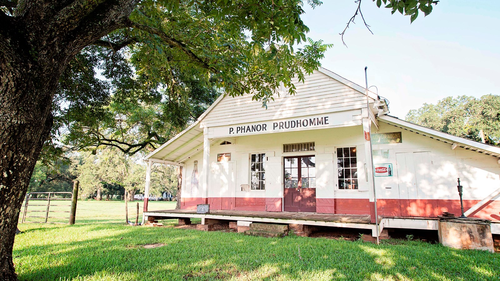 A white and red building with a gable roof and front porch with green grass and large tree in front.
