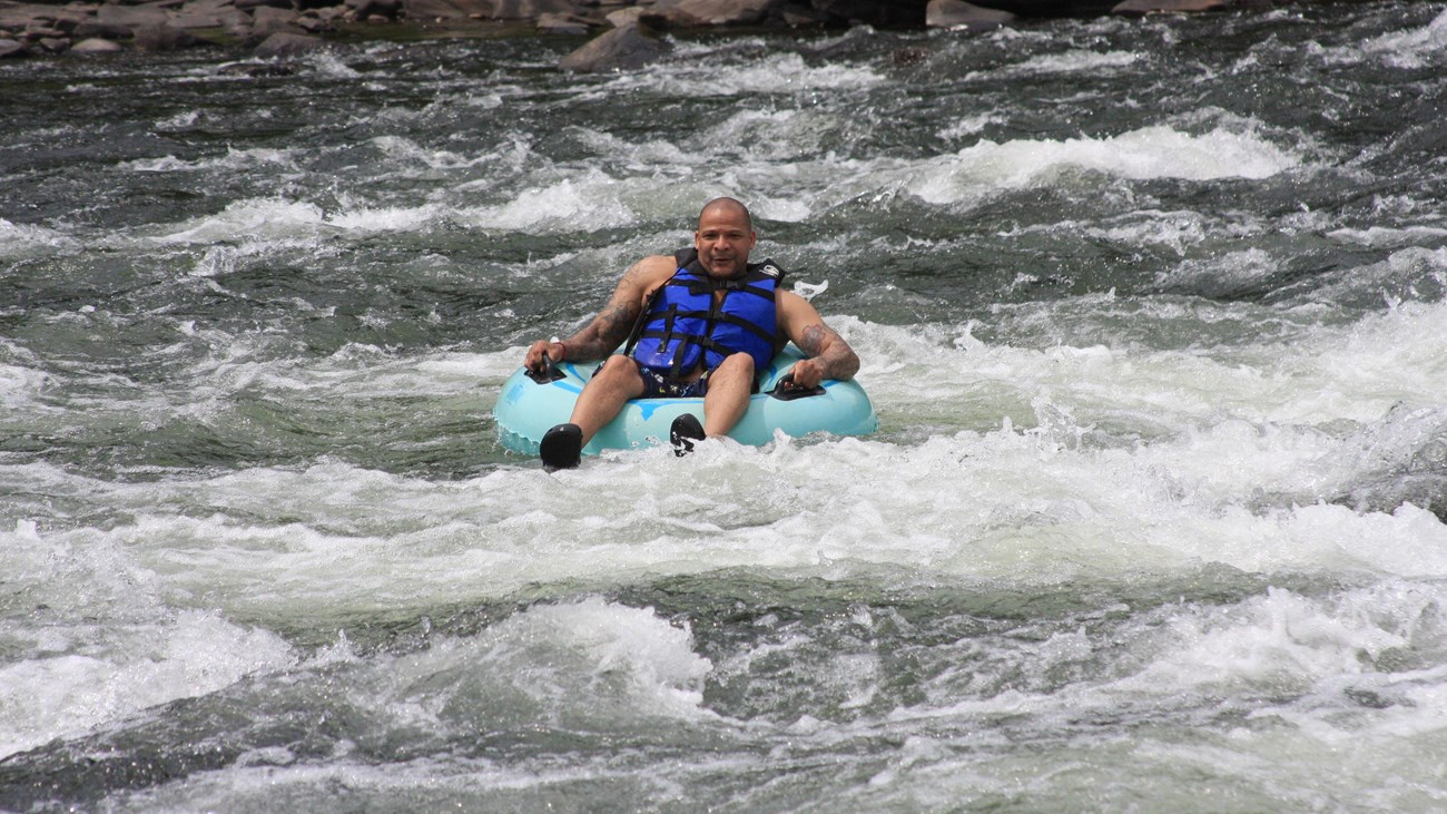 man in life jacket and blue inner tube floats through white-water rapids