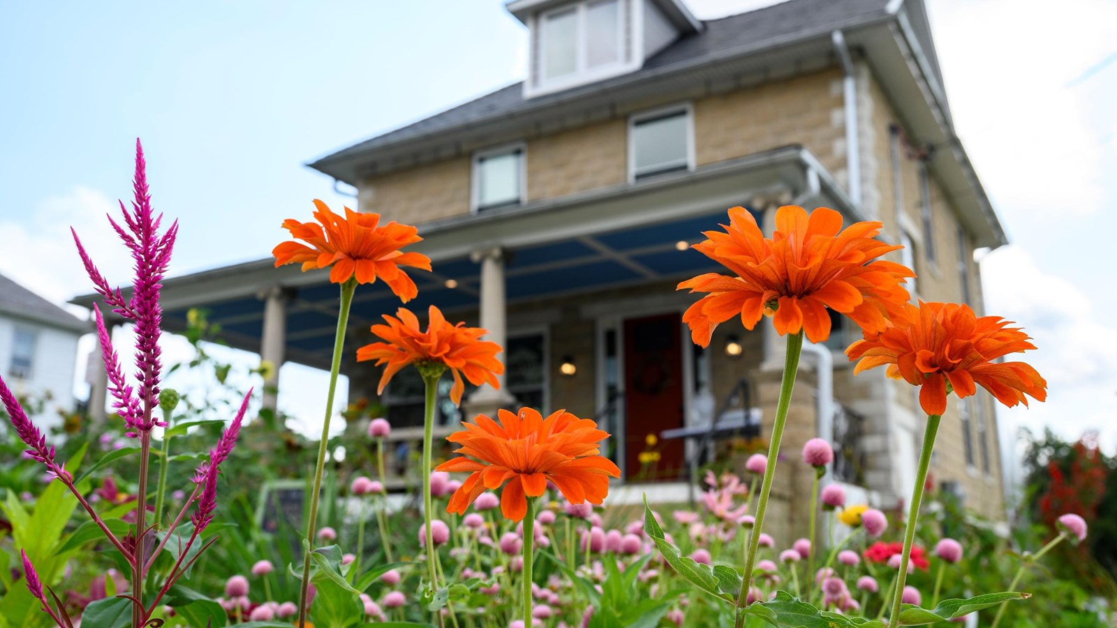 Orange and pink flowers in a garden with a stone house in the background.