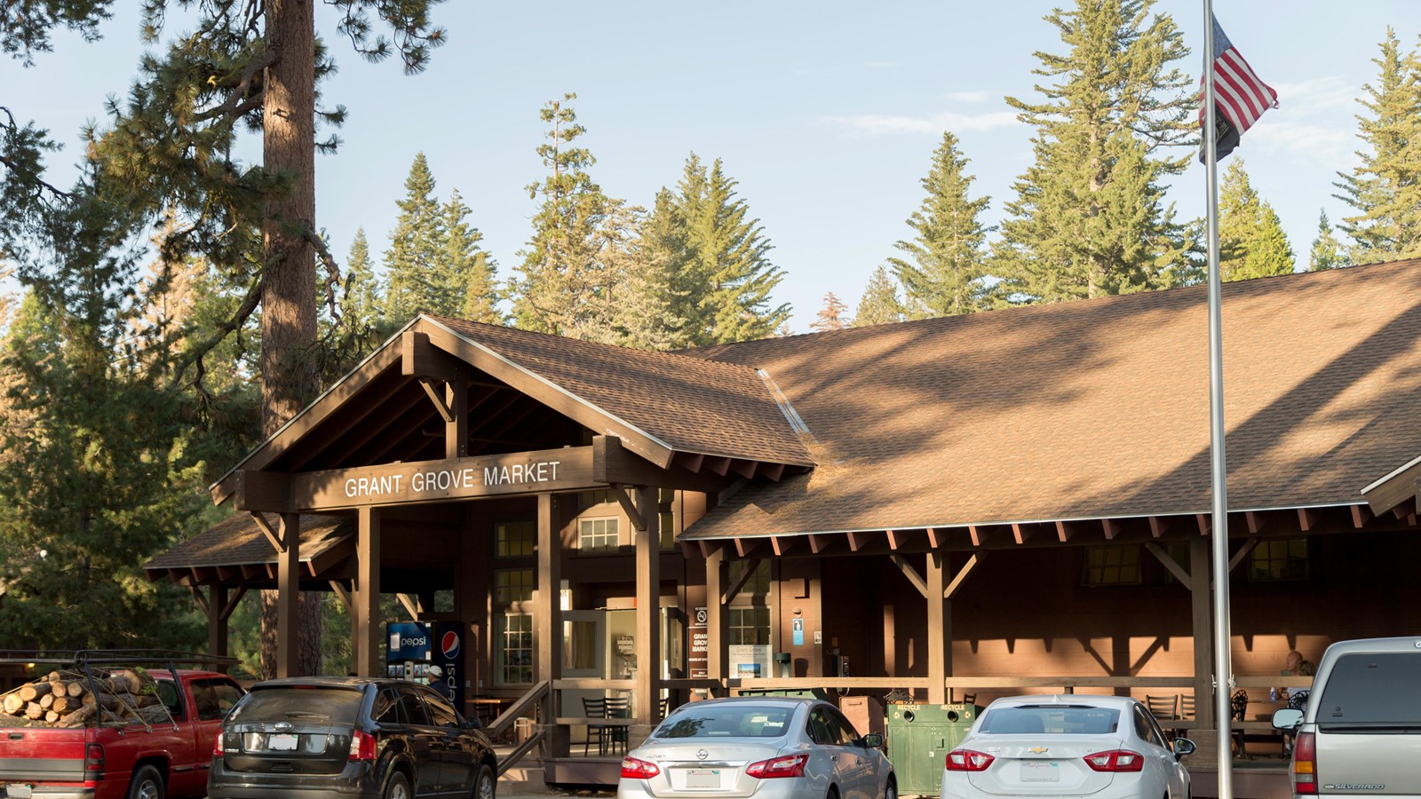 A brown building stands in front of tall green trees. 