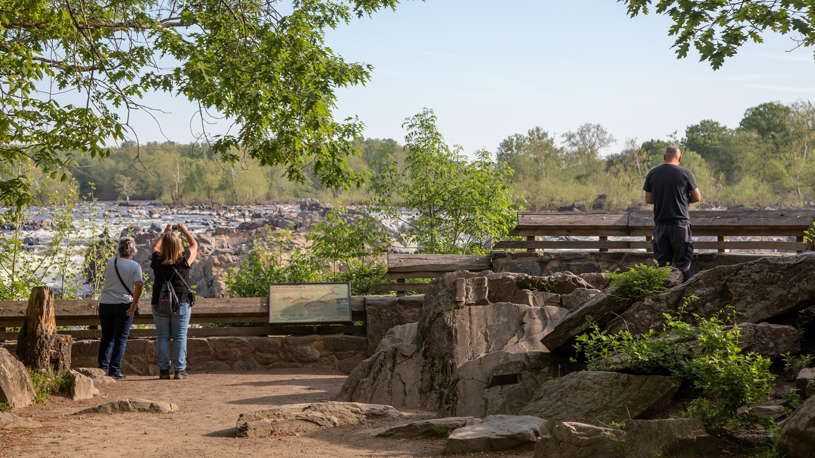 Three people along a wooden railing look down on a rocky waterfall.