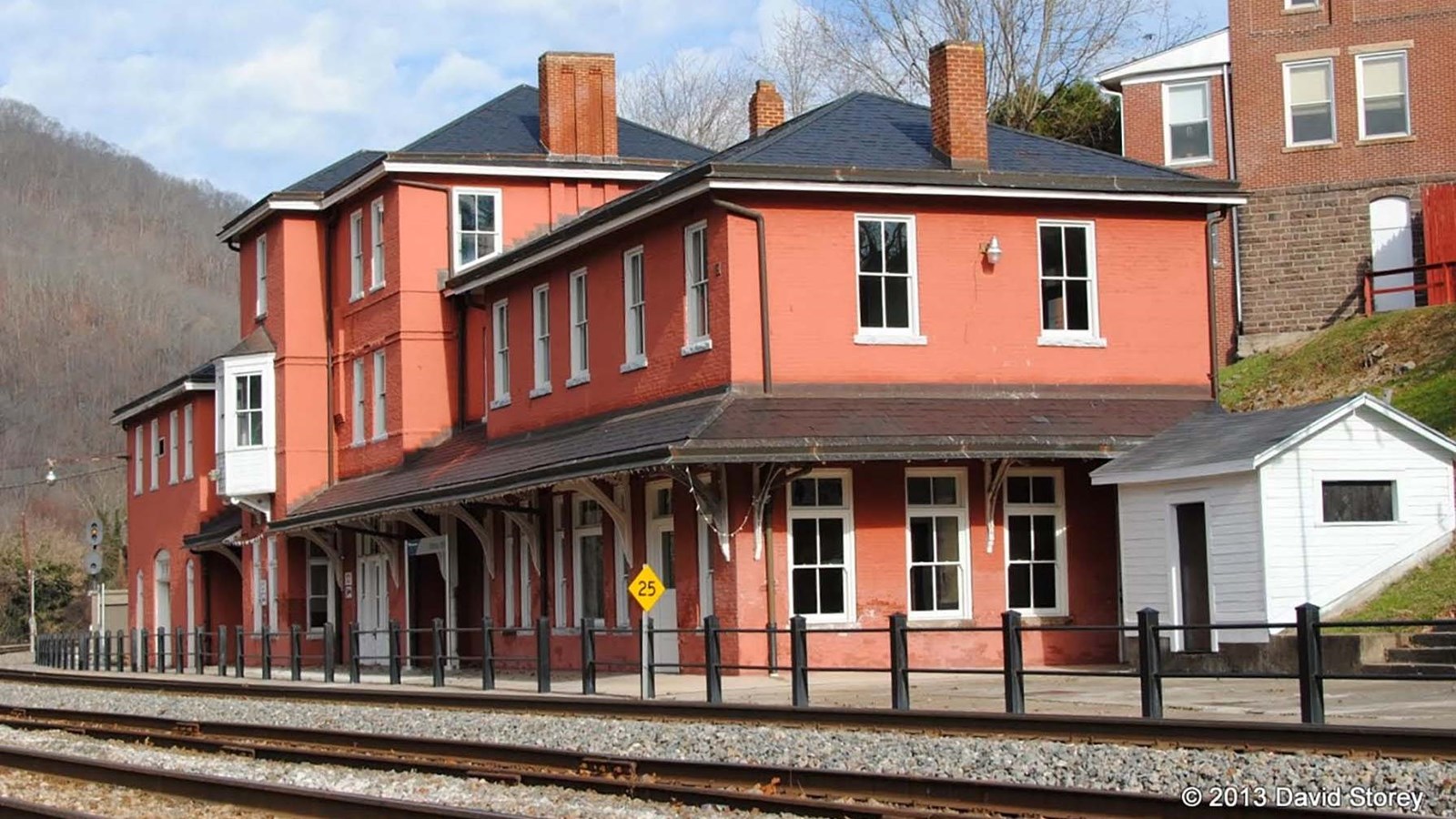 A long red brick railroad depot next to a railroad track.