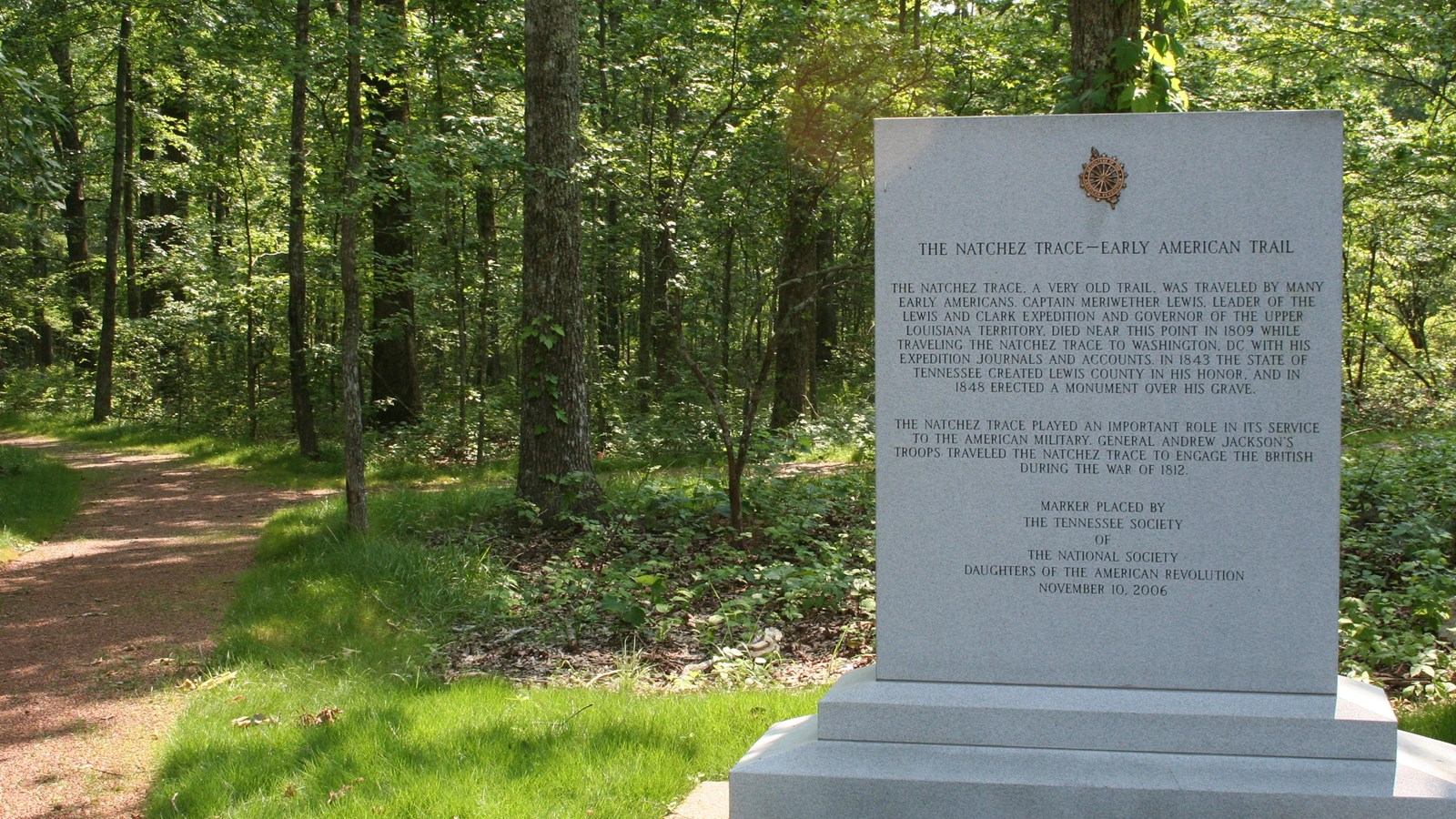 Granite DAR Marker on edge of forest. Green grass surrounds the monument at the edge of the forest.