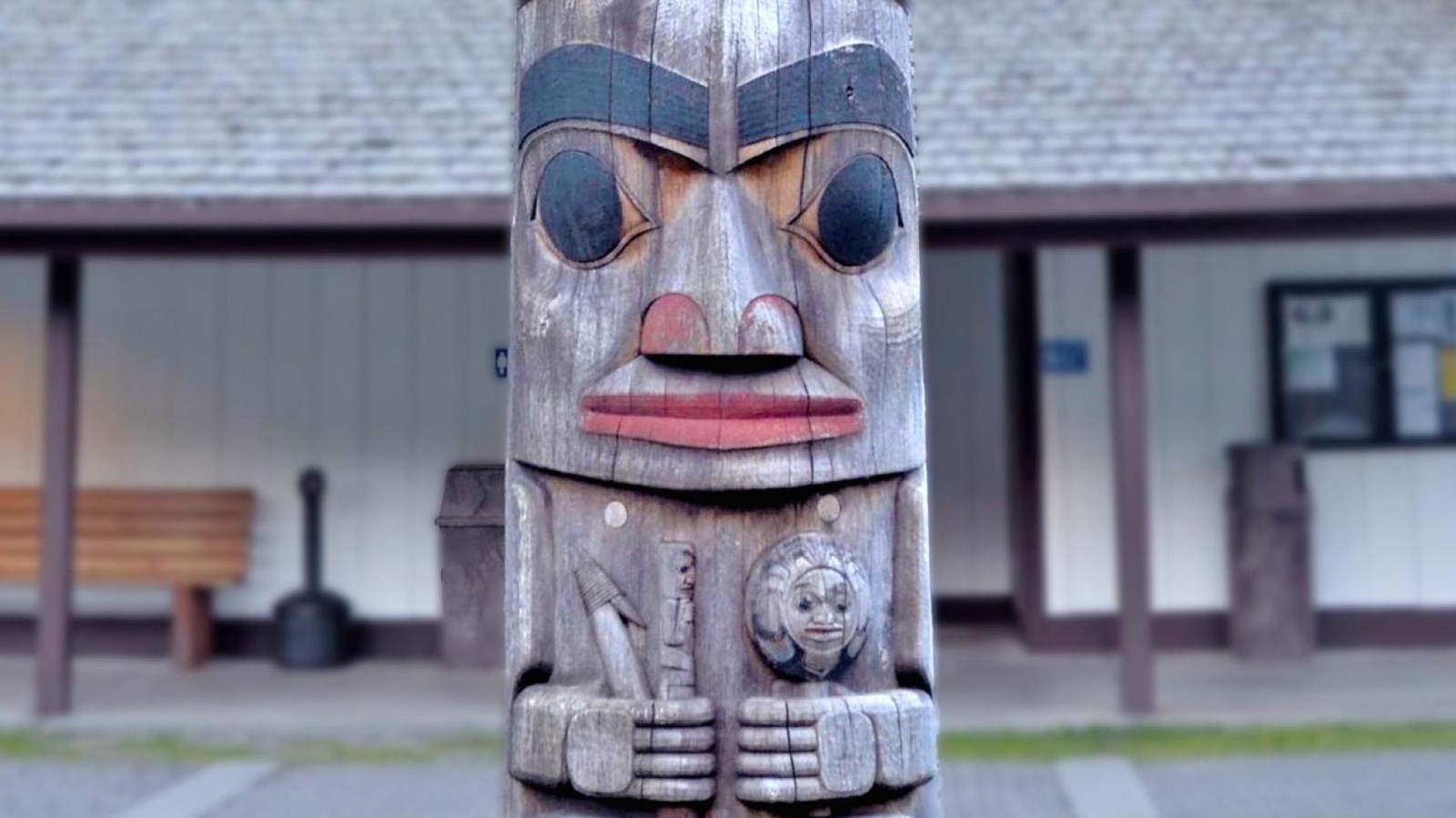 Close up of a portion of a totem pole with a building in the background