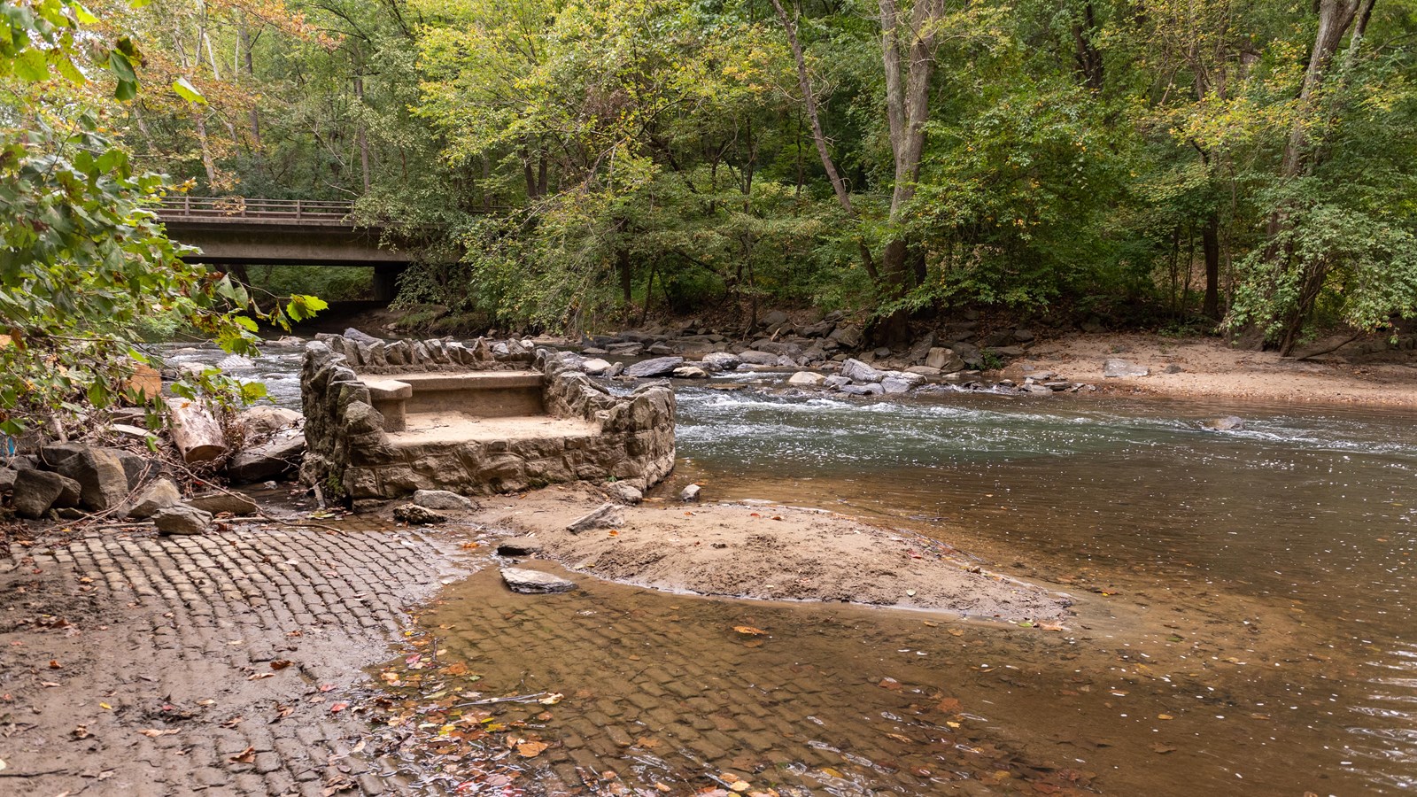 An embankment next to a river surrounded by woods. 