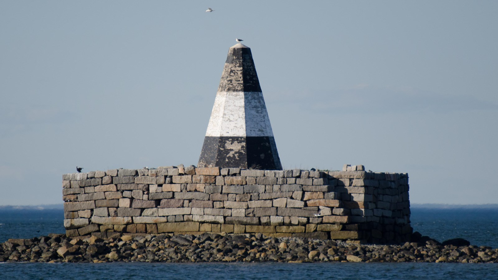 View from the water of a black and white triangle stick up from a platform built out of stone