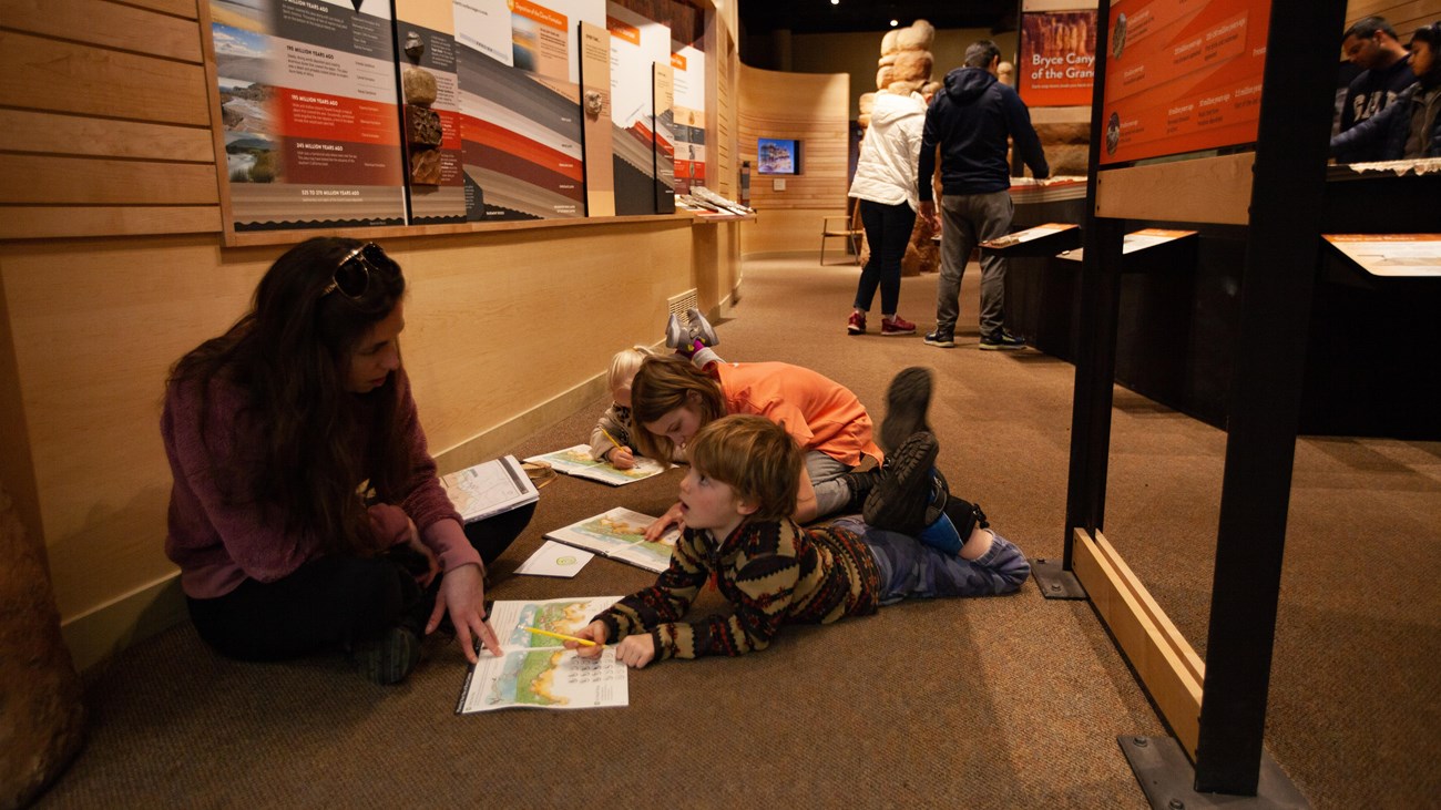 Three children and an adult sit on the floor working on an activity book