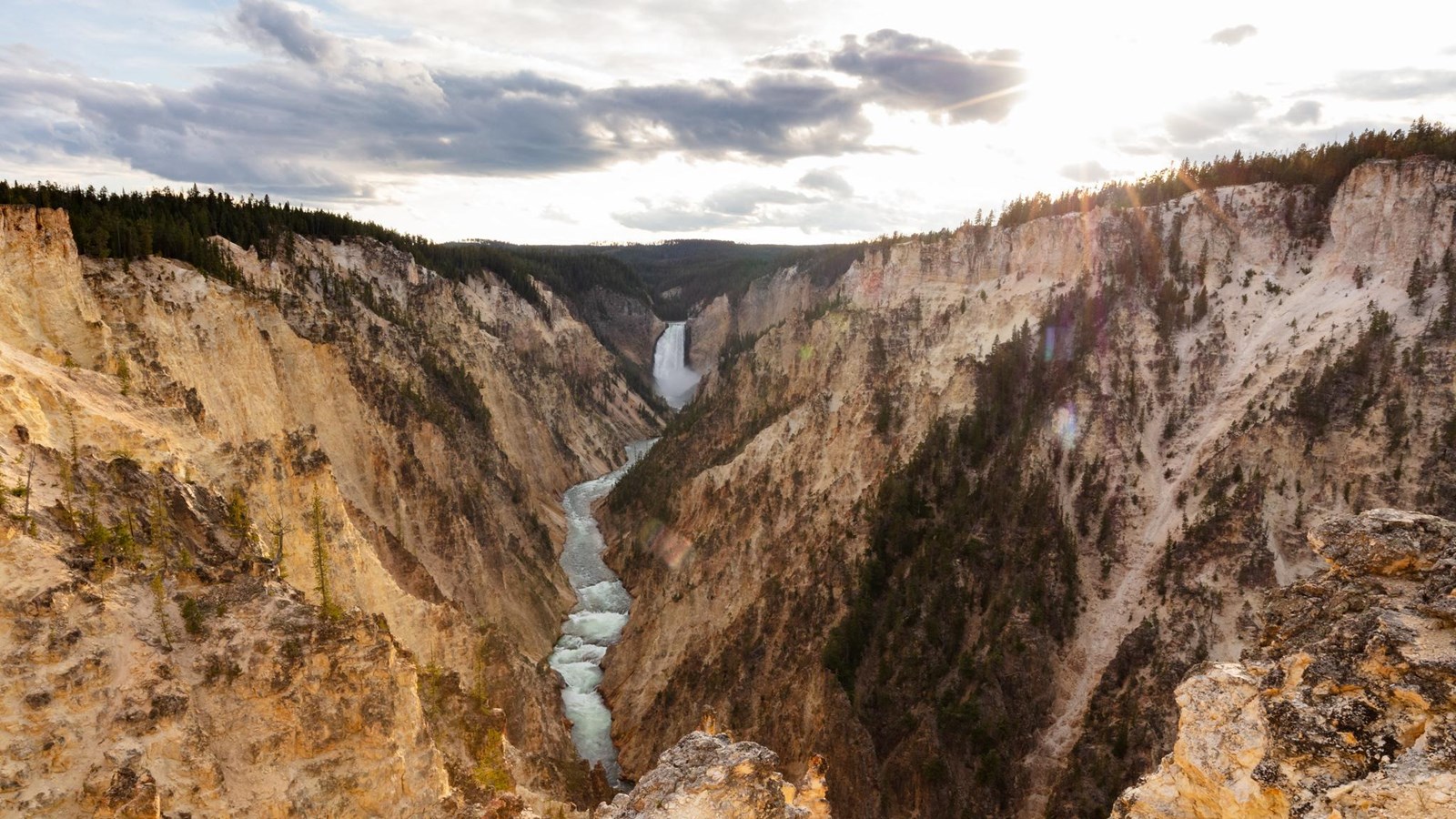 The sun sets over a canyon with steep, pale yellow walls and a 300 ft waterfall.