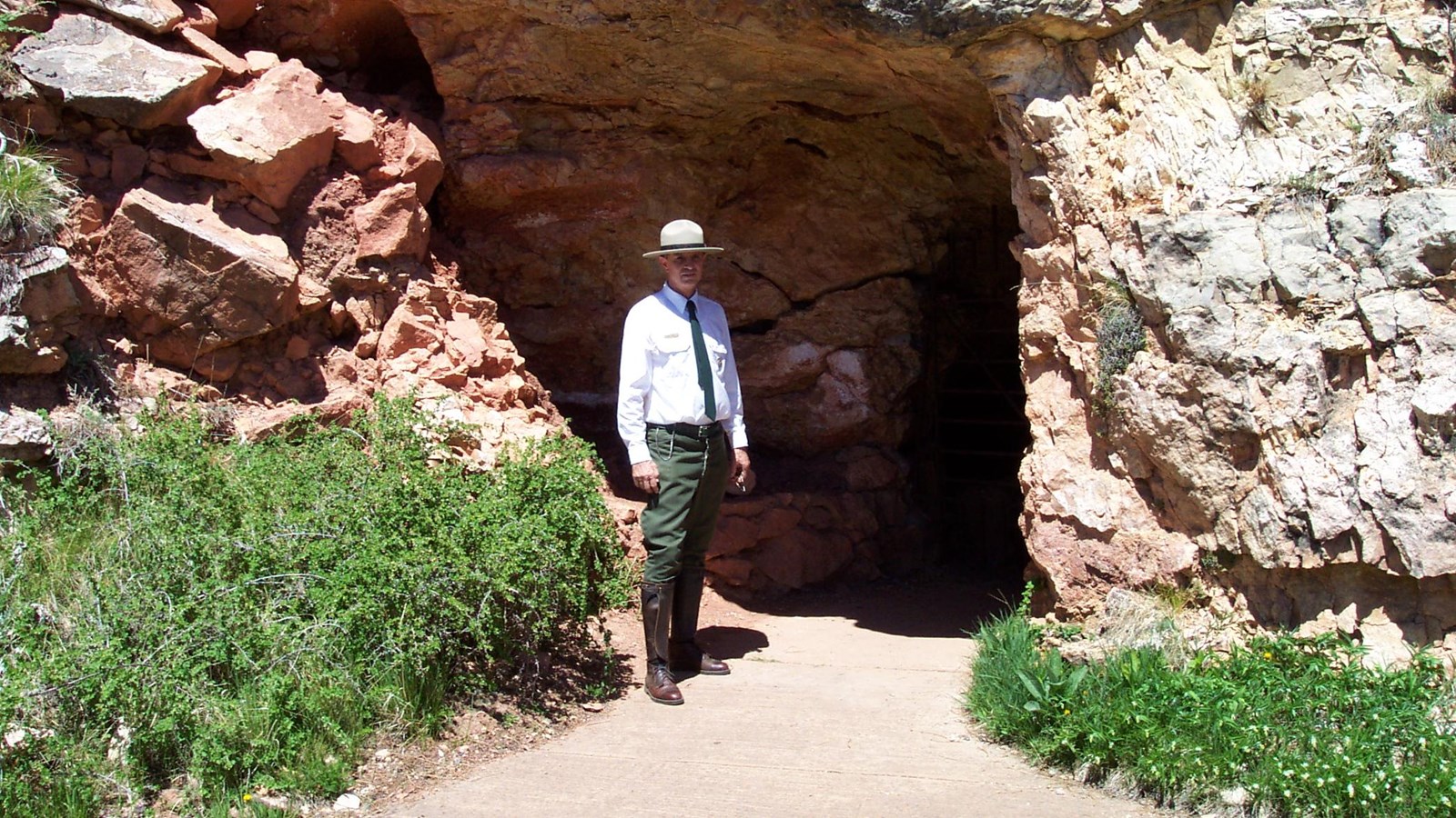 Ranger standing in front of opening in limestone cliff.