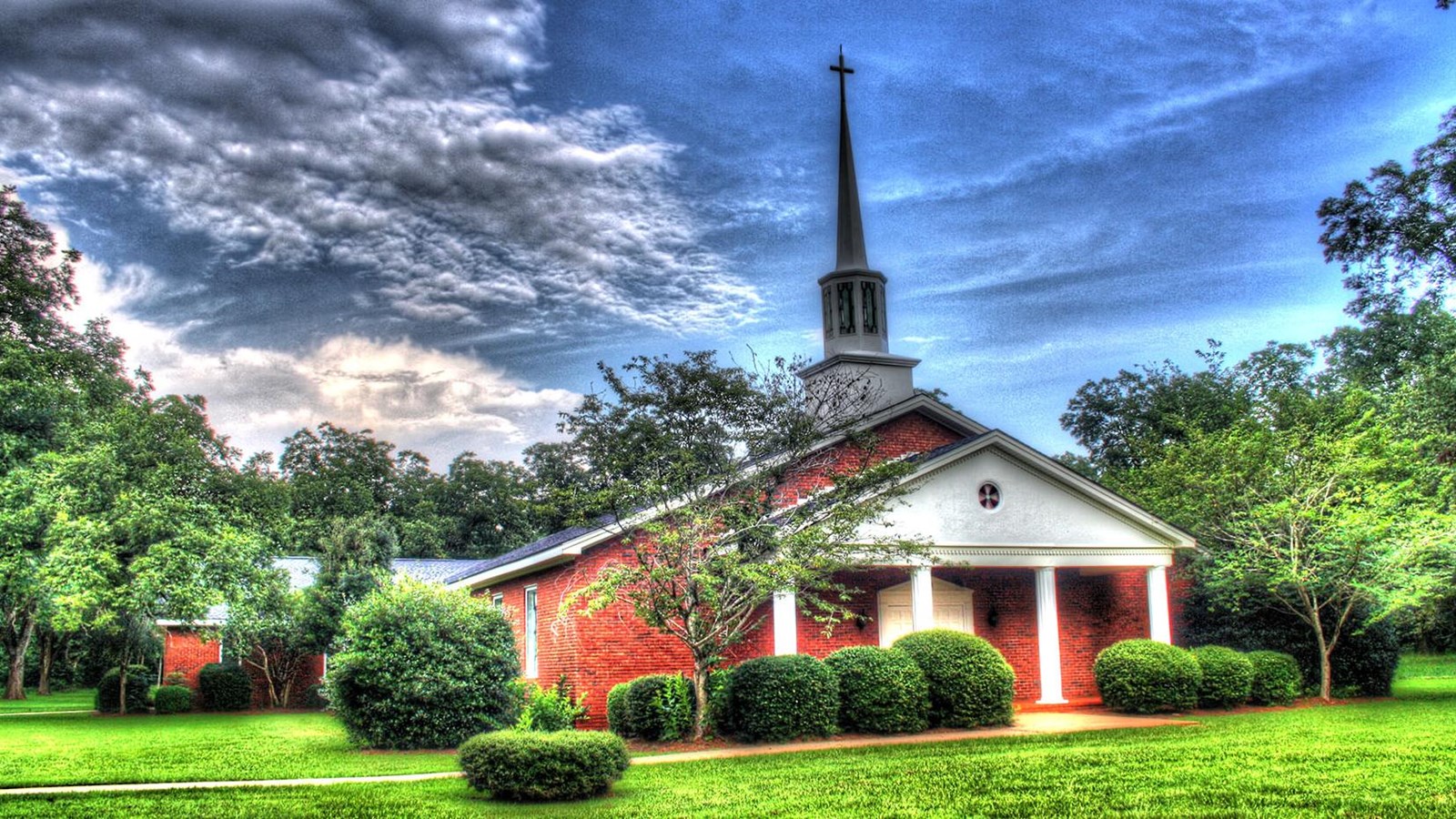 a one story red brick church with a tall white spire