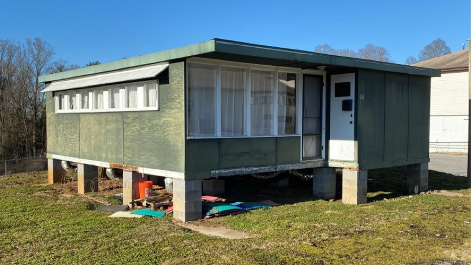 A small green house with flat roof sits on cinder blocks.