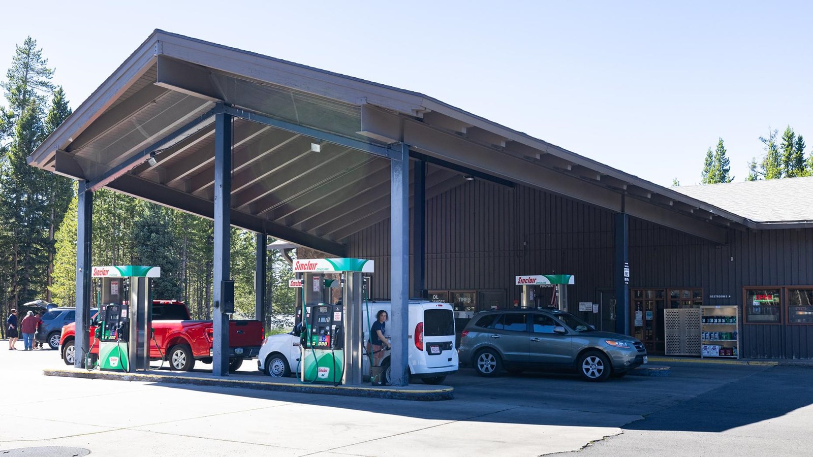 Four gas pumps sit underneath the protective roof of a brown, metal building.