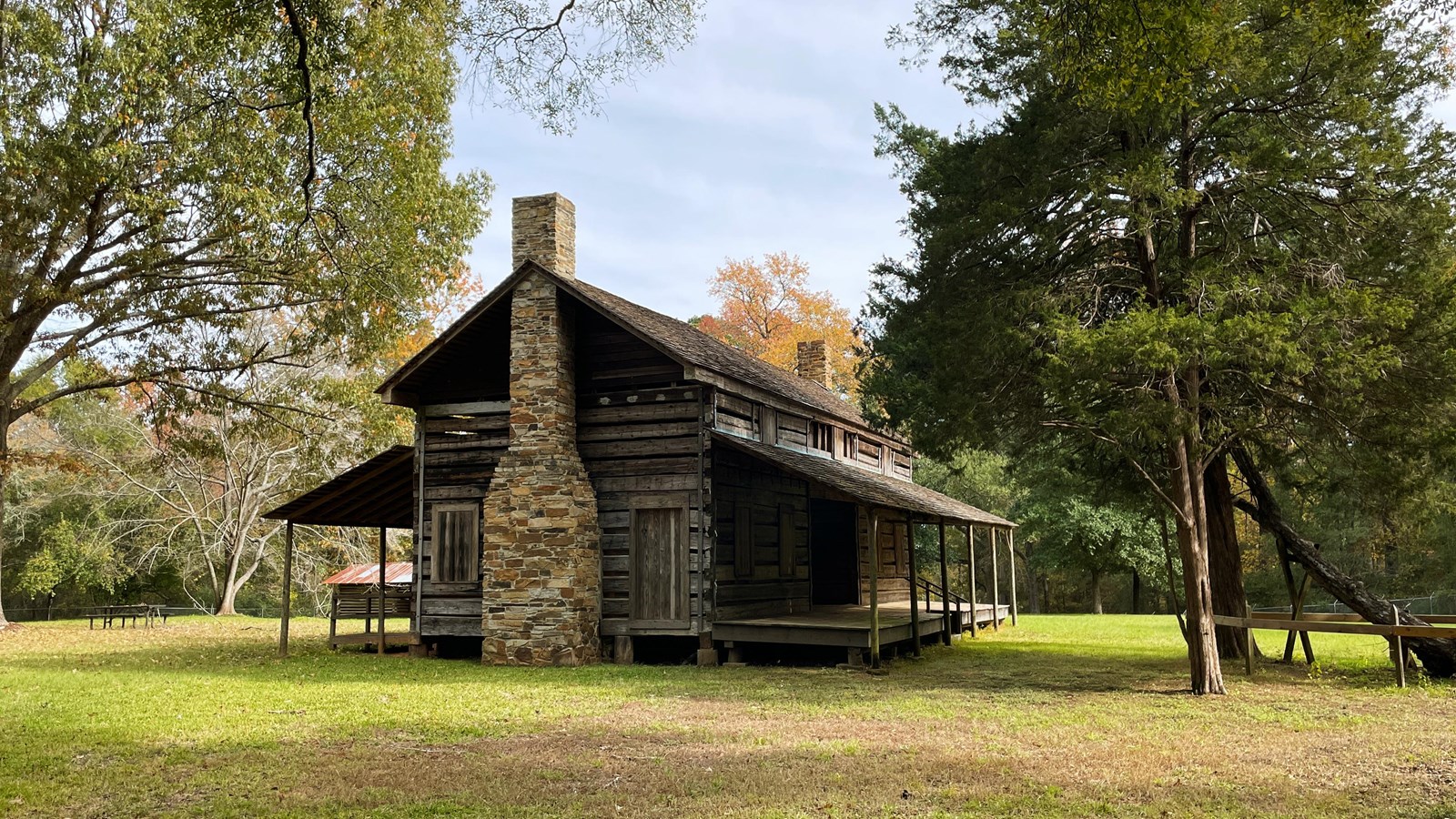 A one and a half story log plank home with stone fireplaces on either end and porches on the front a