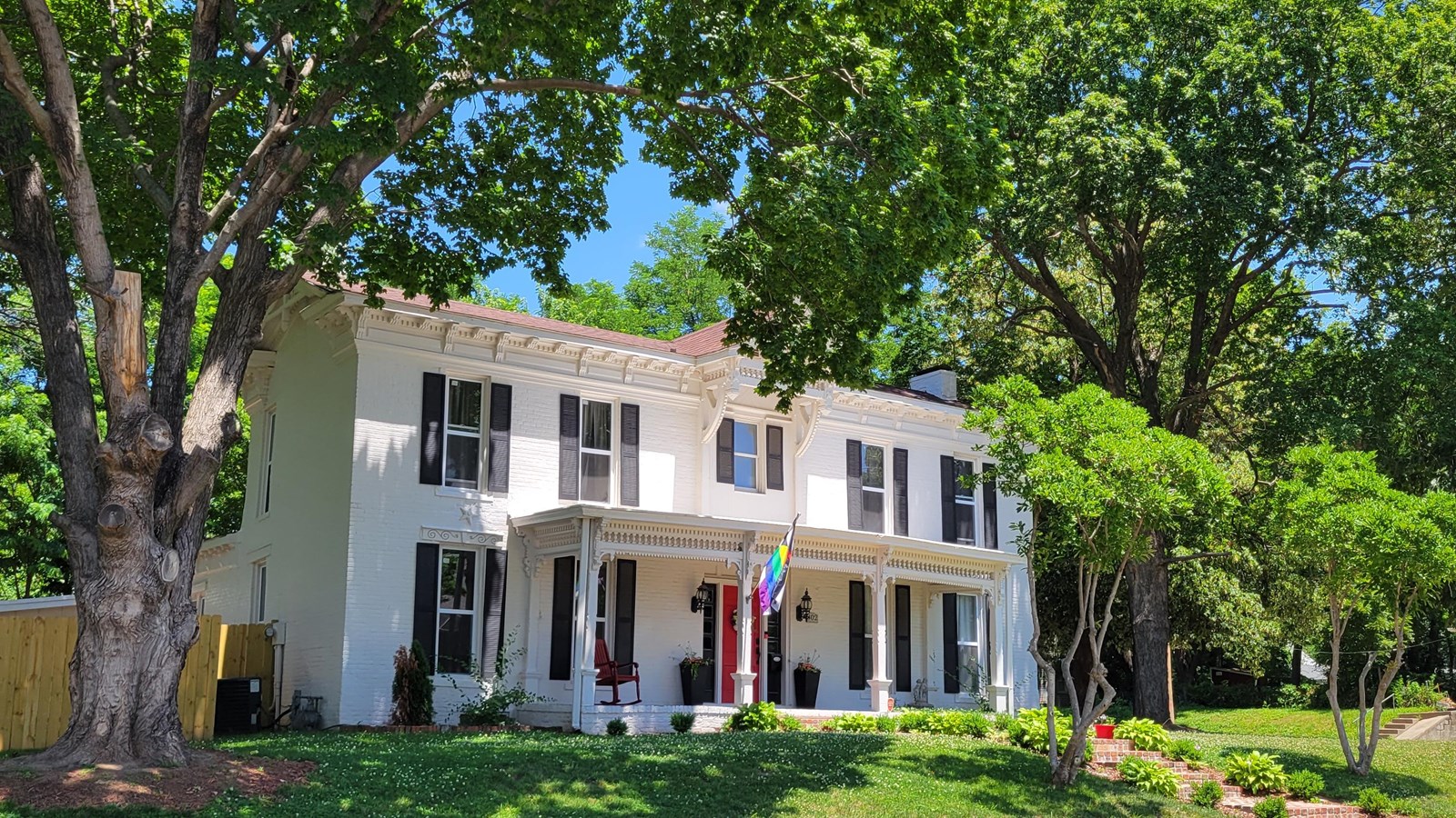 Large, white, two-story colonial home between two large trees. 