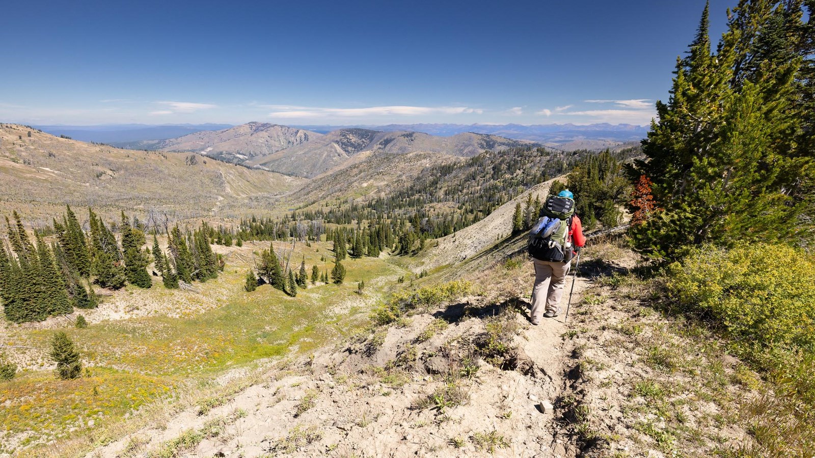 A person hikes along a ridgeline with mountains in the distance.