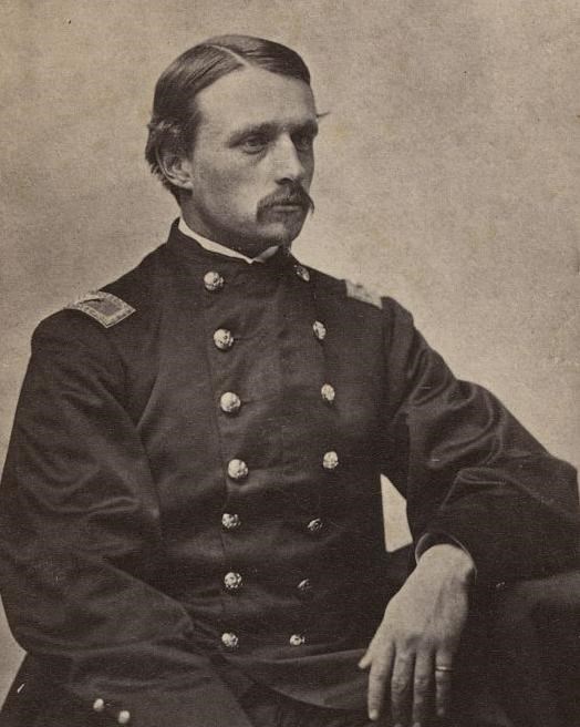 young man with short hair and mustache in civil war era U.S. army uniform sitting at a desk.