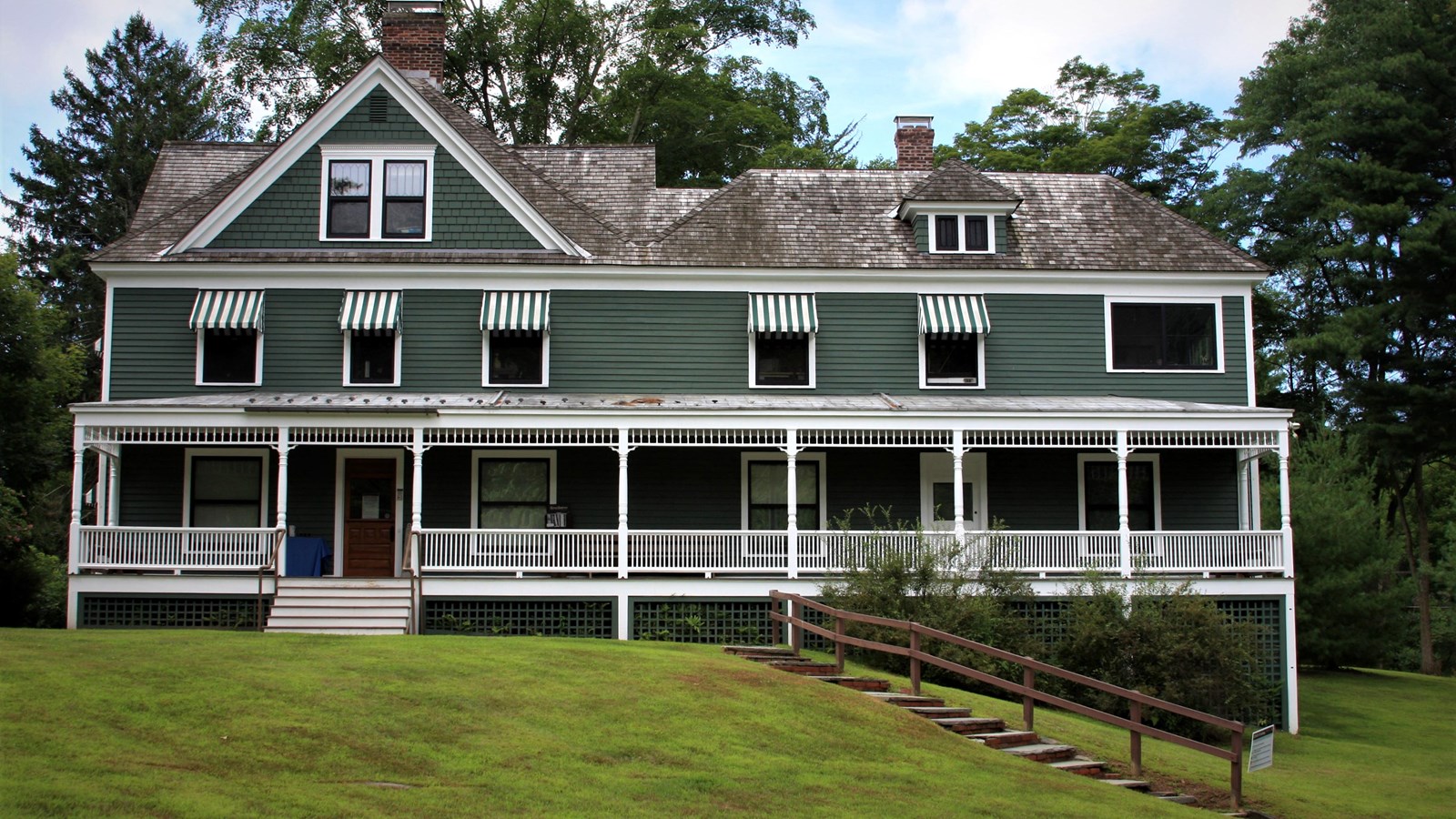 2 story gray-green house with white trim, wraparound white porch with roof, and wood shingle roof