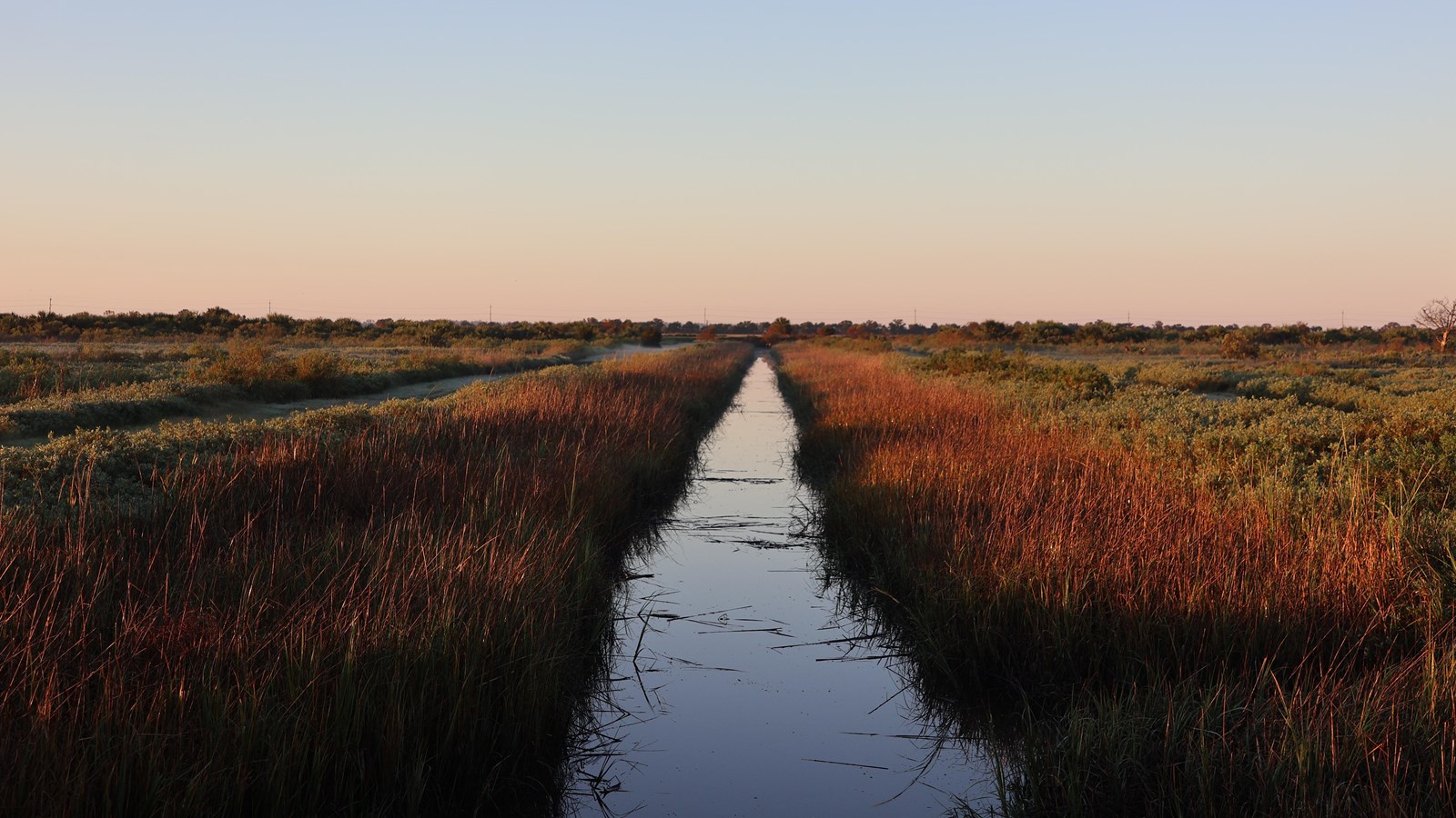 An early morning image of a long narrow canal with grass along the edges. 