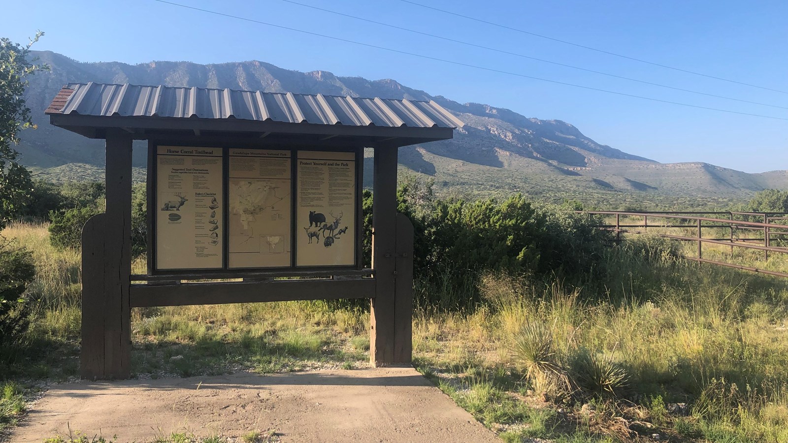 A wood kiosk with trail information in front of a desert mountain landscape