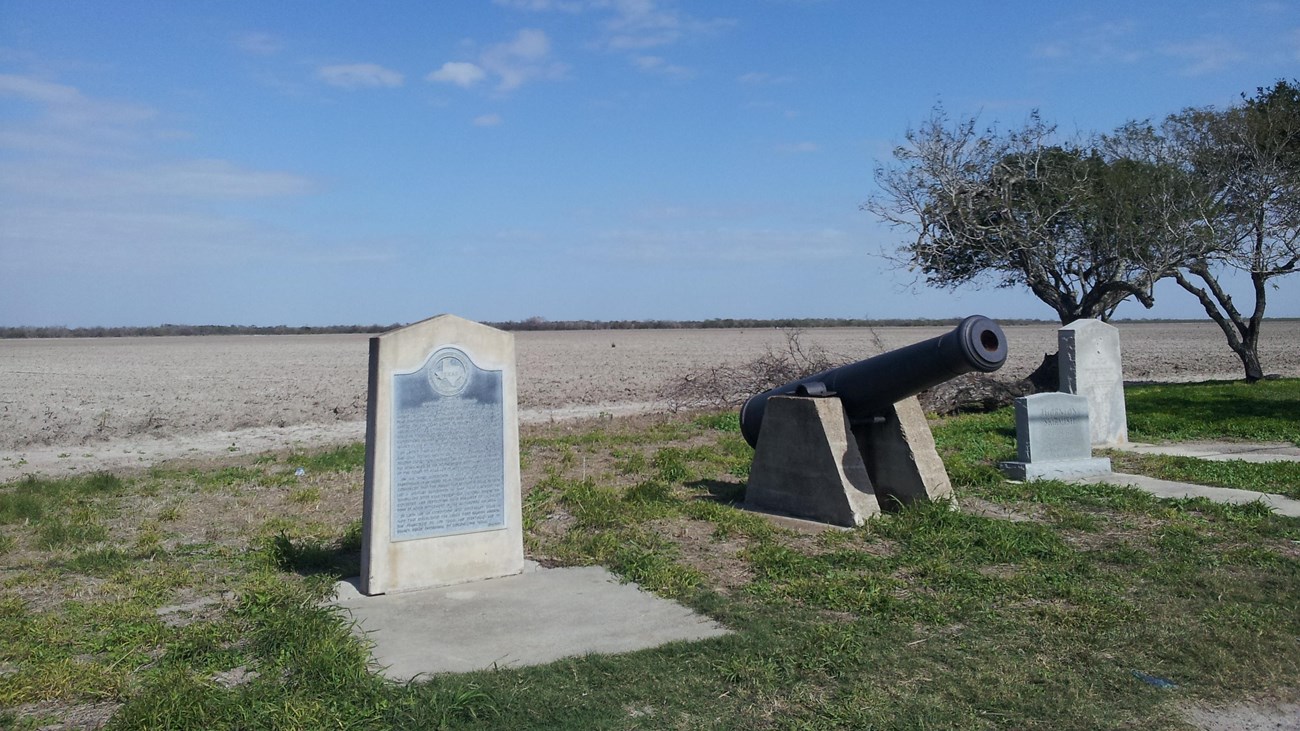Concrete historical maker next to black siege cannon on concrete base.