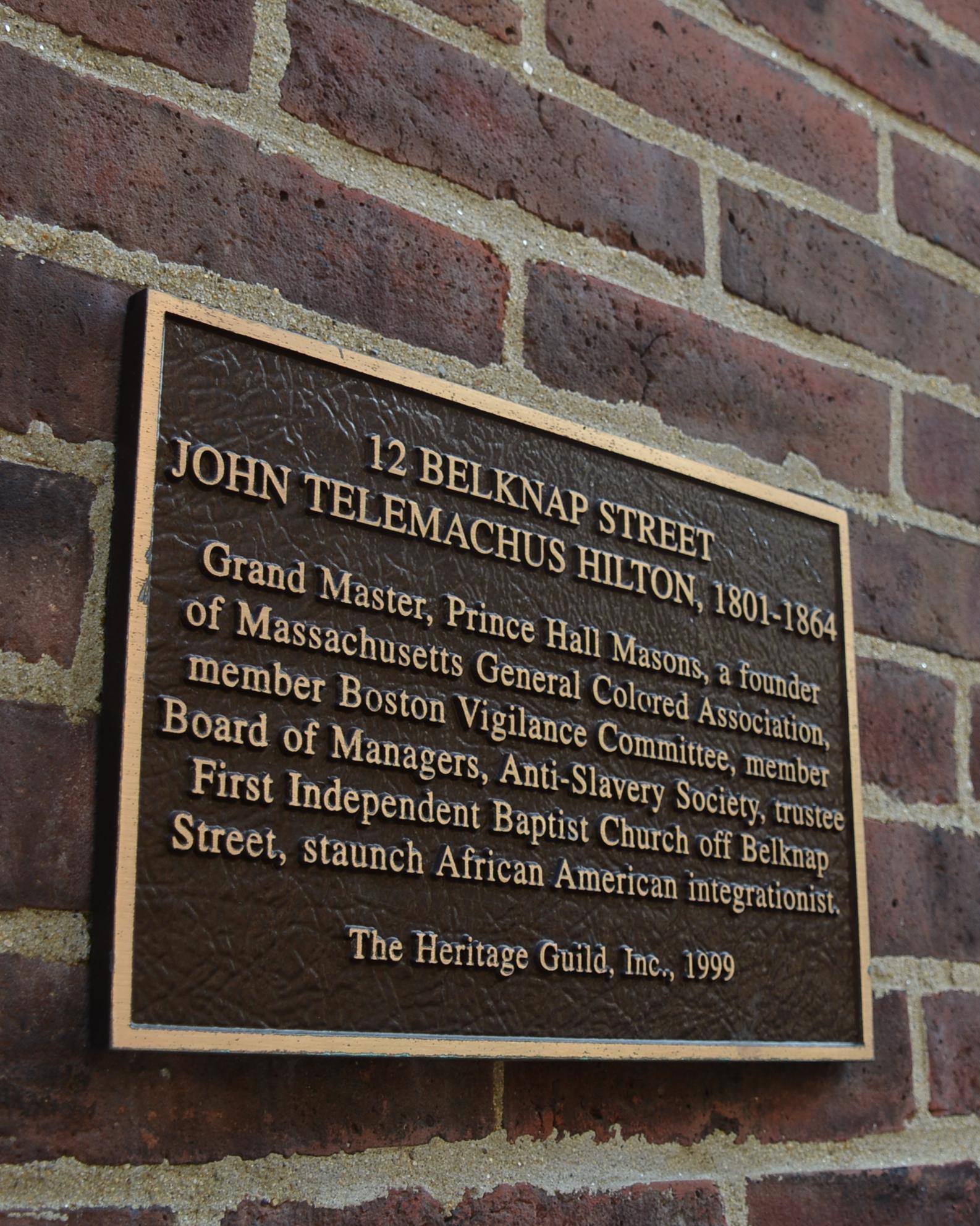Historic plaque on a brick wall identifying the home of John T. Hilton at 12 Belknap Street.