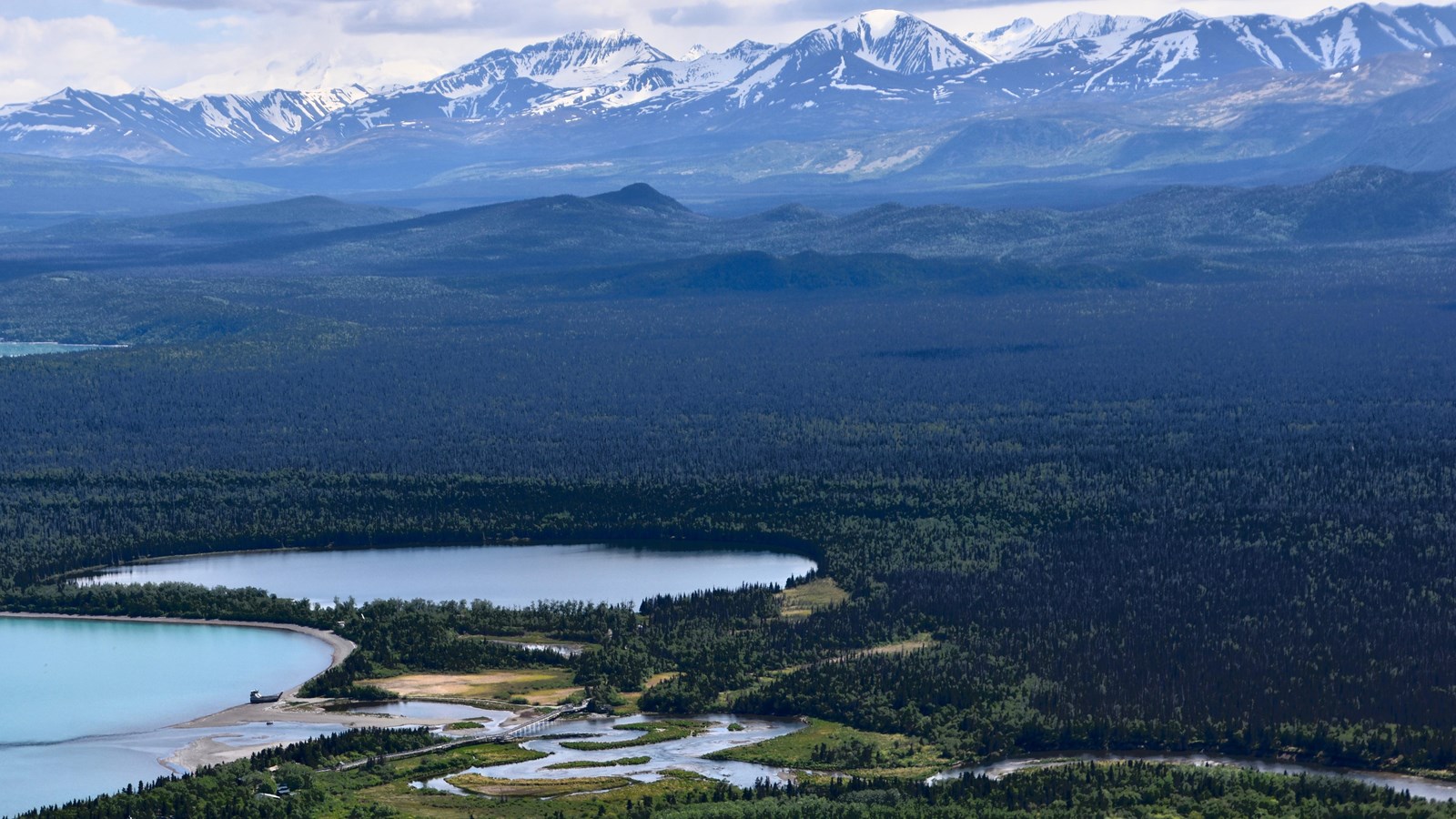 Looking down on a developed area with several buildings and a river with mountains in the background
