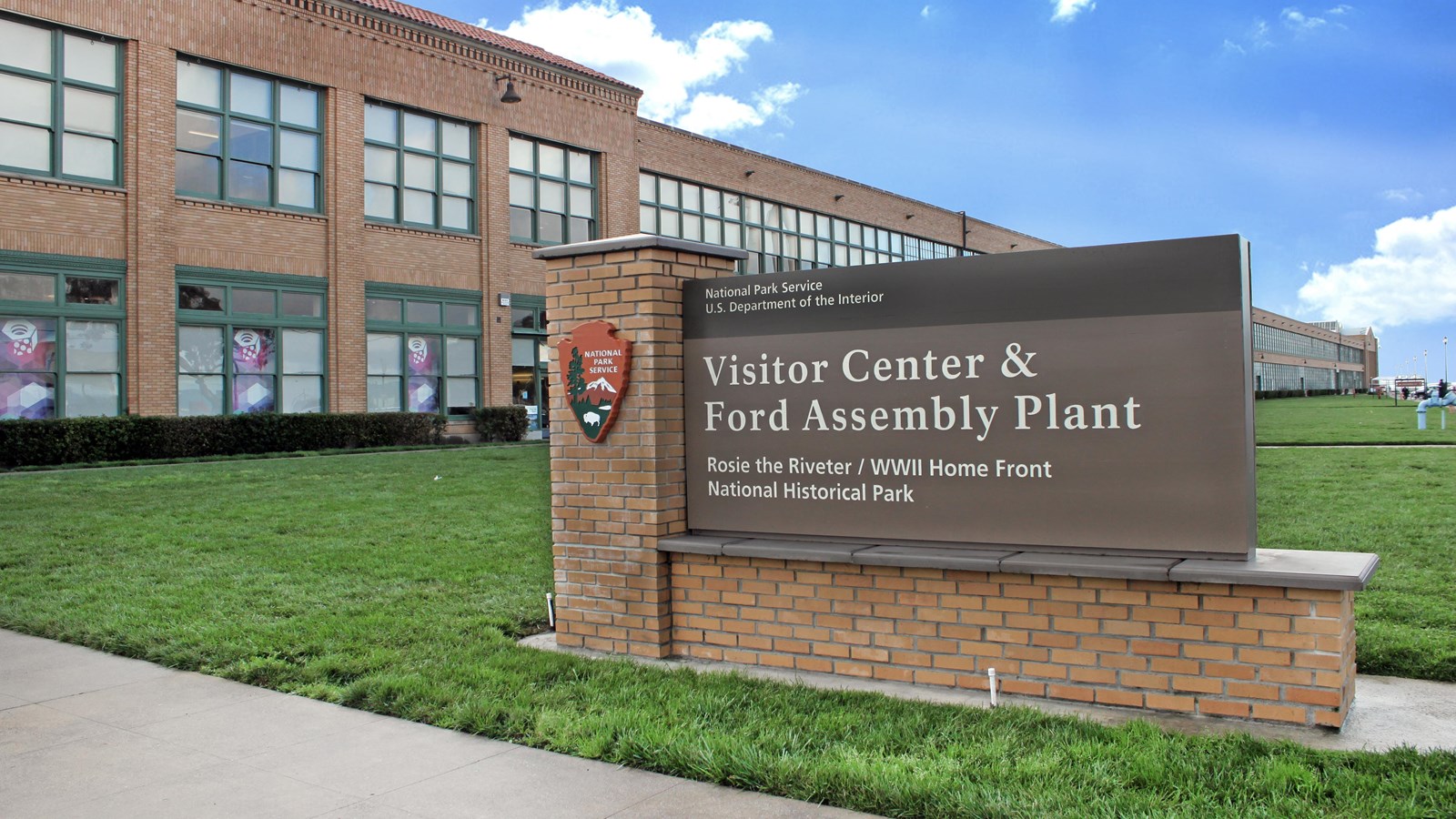 A brick entrance sign sets in front of a large brick building. 