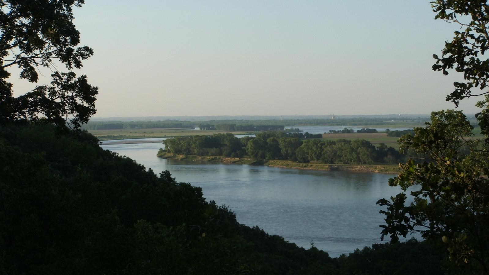 Photo with dark woods and underbrush framing a view of the Missouri River at sunset.