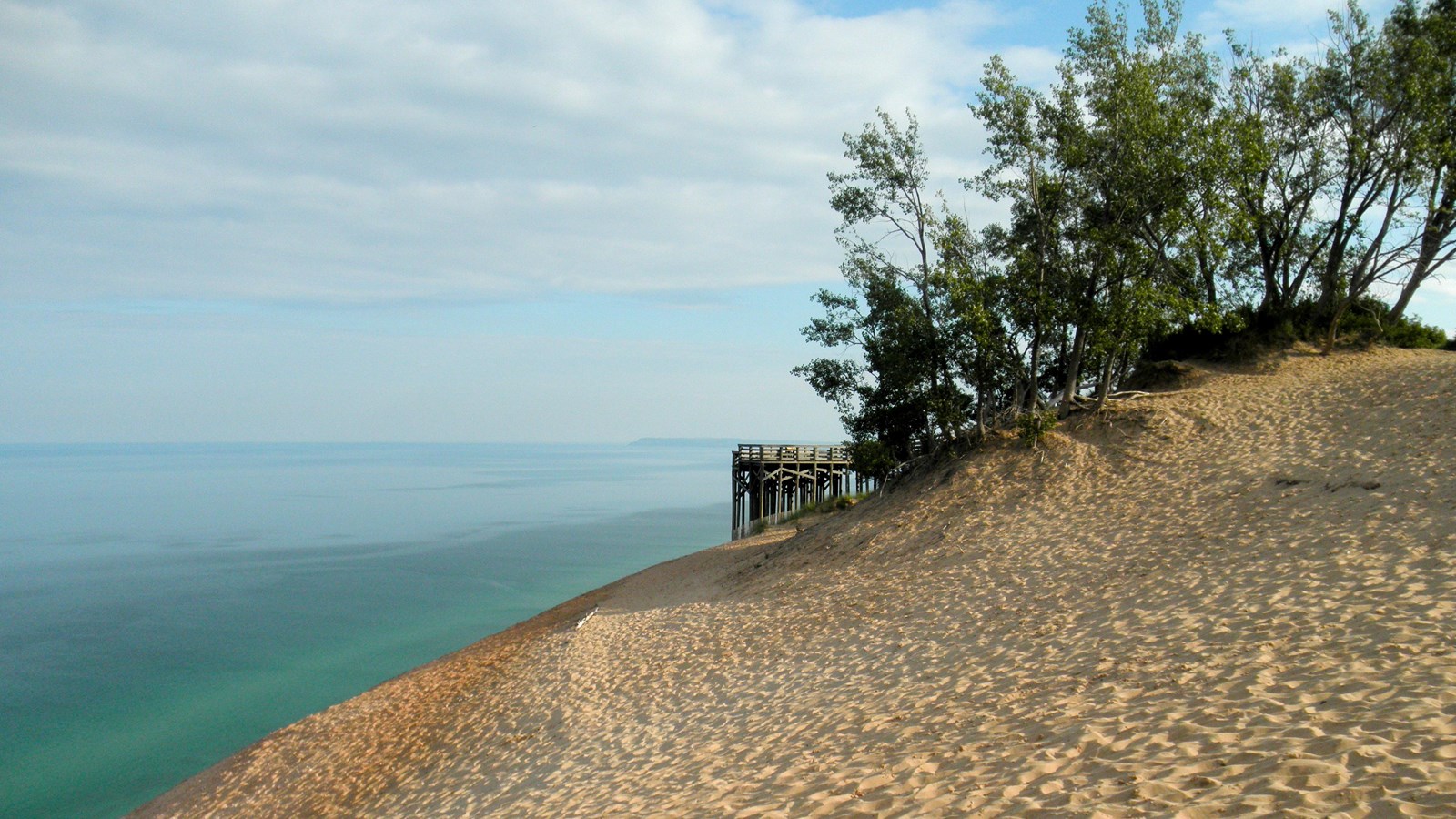 Wooden overlook platform nestled in trees at edge of dune bluff with turquoise water behind