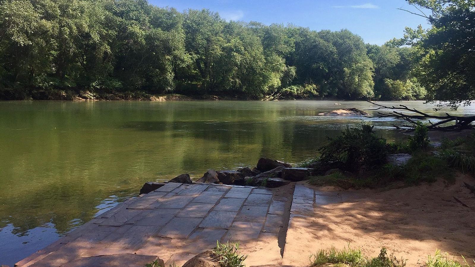 View looking upstream at the steps leading into the river with wooded shoreline in the distance.