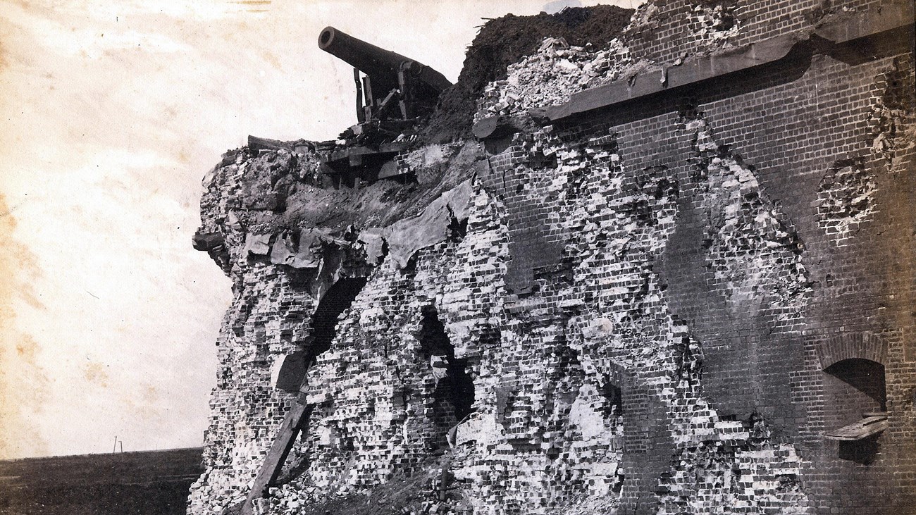 A destroyed brick wall with a cannon on top hanging over the edge. 